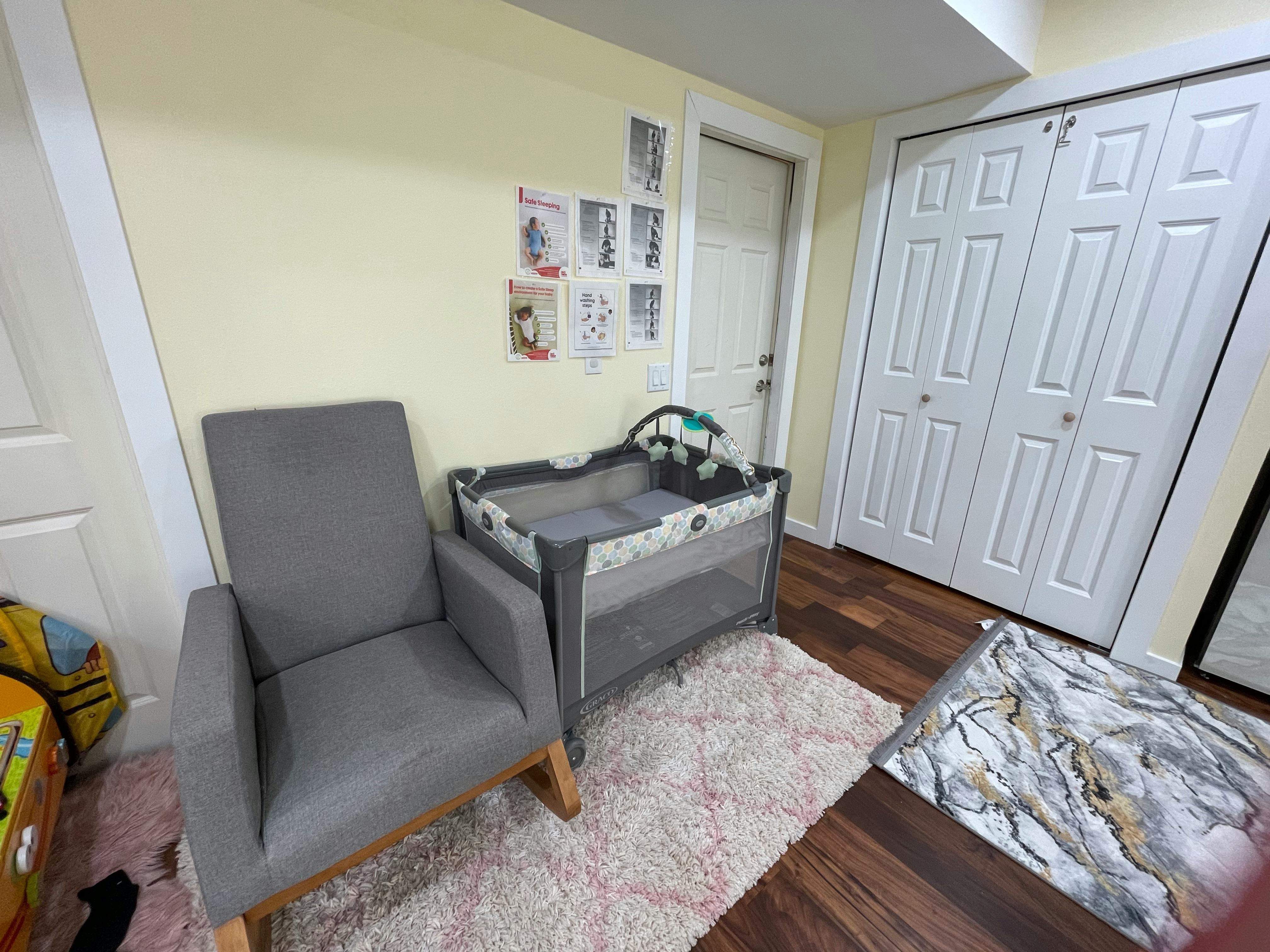 Nursery room with a gray armchair, playpen, and white closet doors