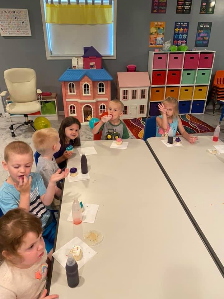 Children sitting at tables with cupcakes and frosting bottles