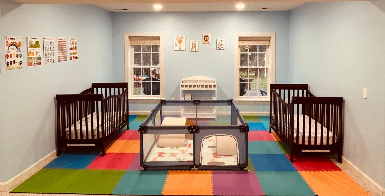 Two cribs and a playpen on a colorful foam mat in a nursery