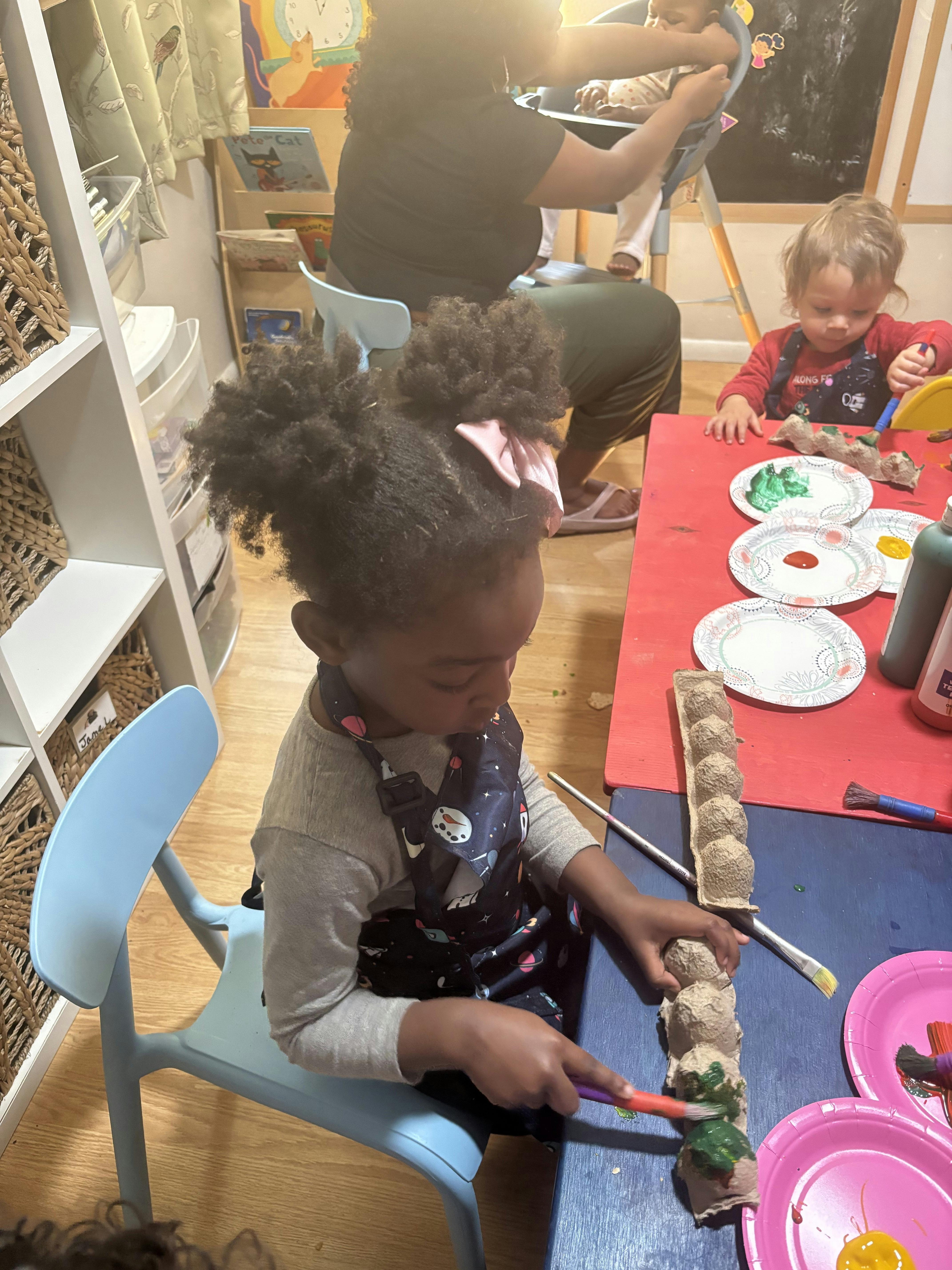 Children wearing aprons painting an egg carton at a table
