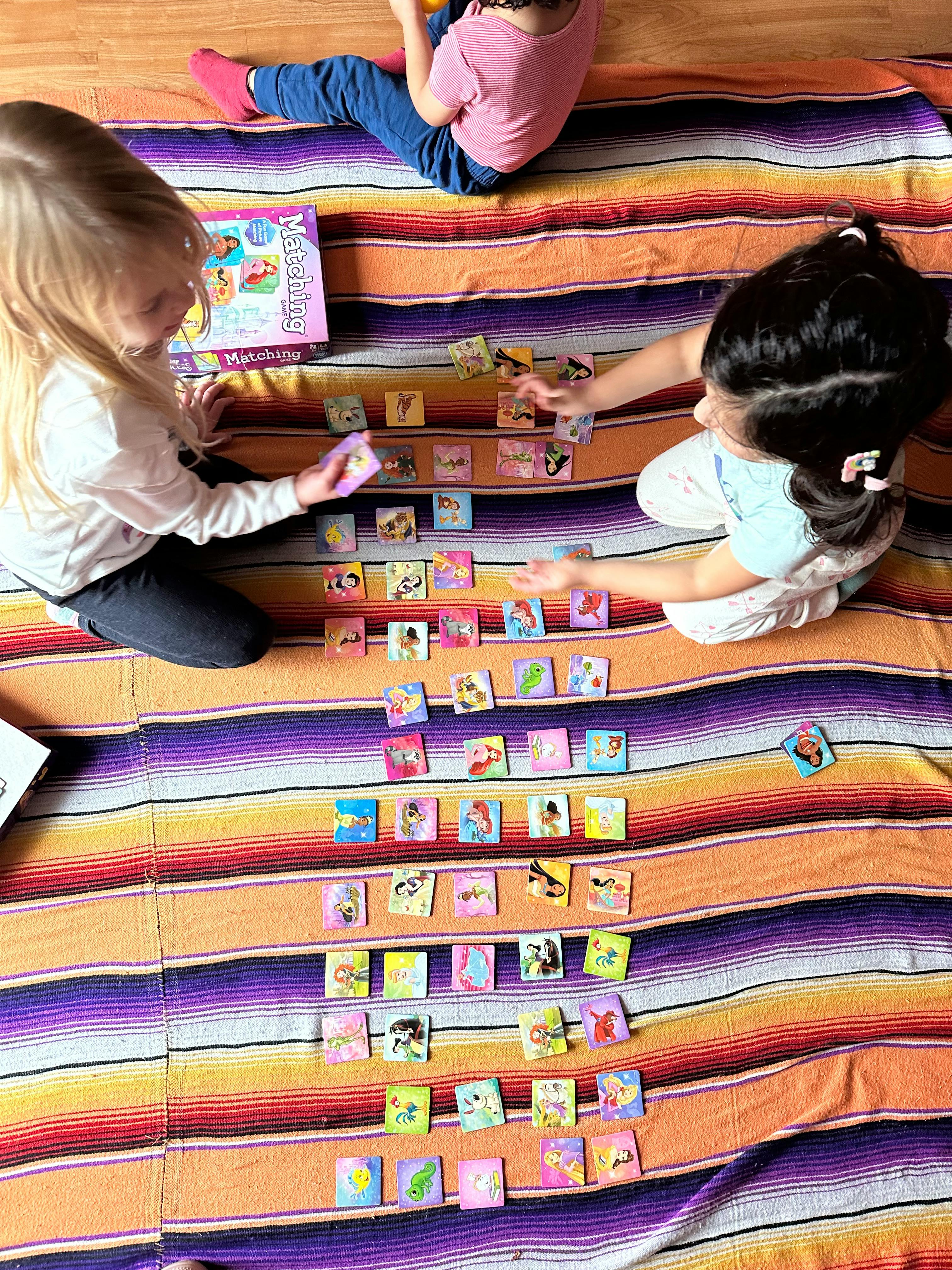 Three children playing a matching game on a striped blanket
