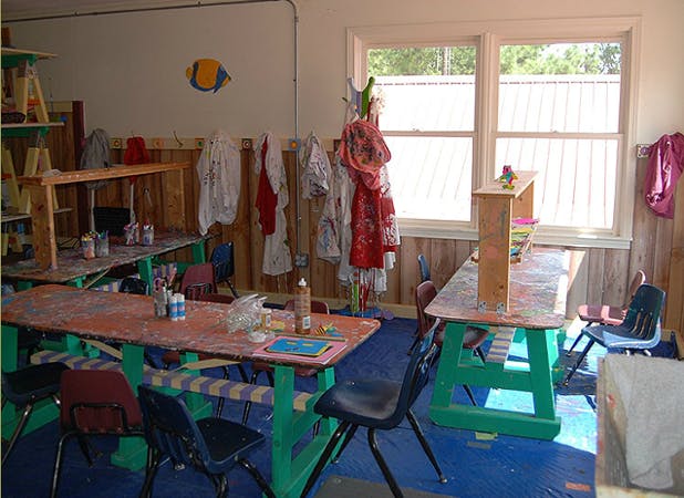 Classroom with tables, chairs, and clothes hanging on a rack