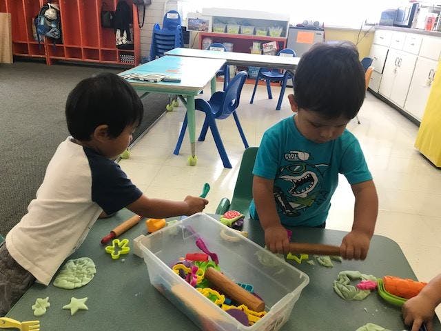 Two children playing with modeling clay at a table in a classroom