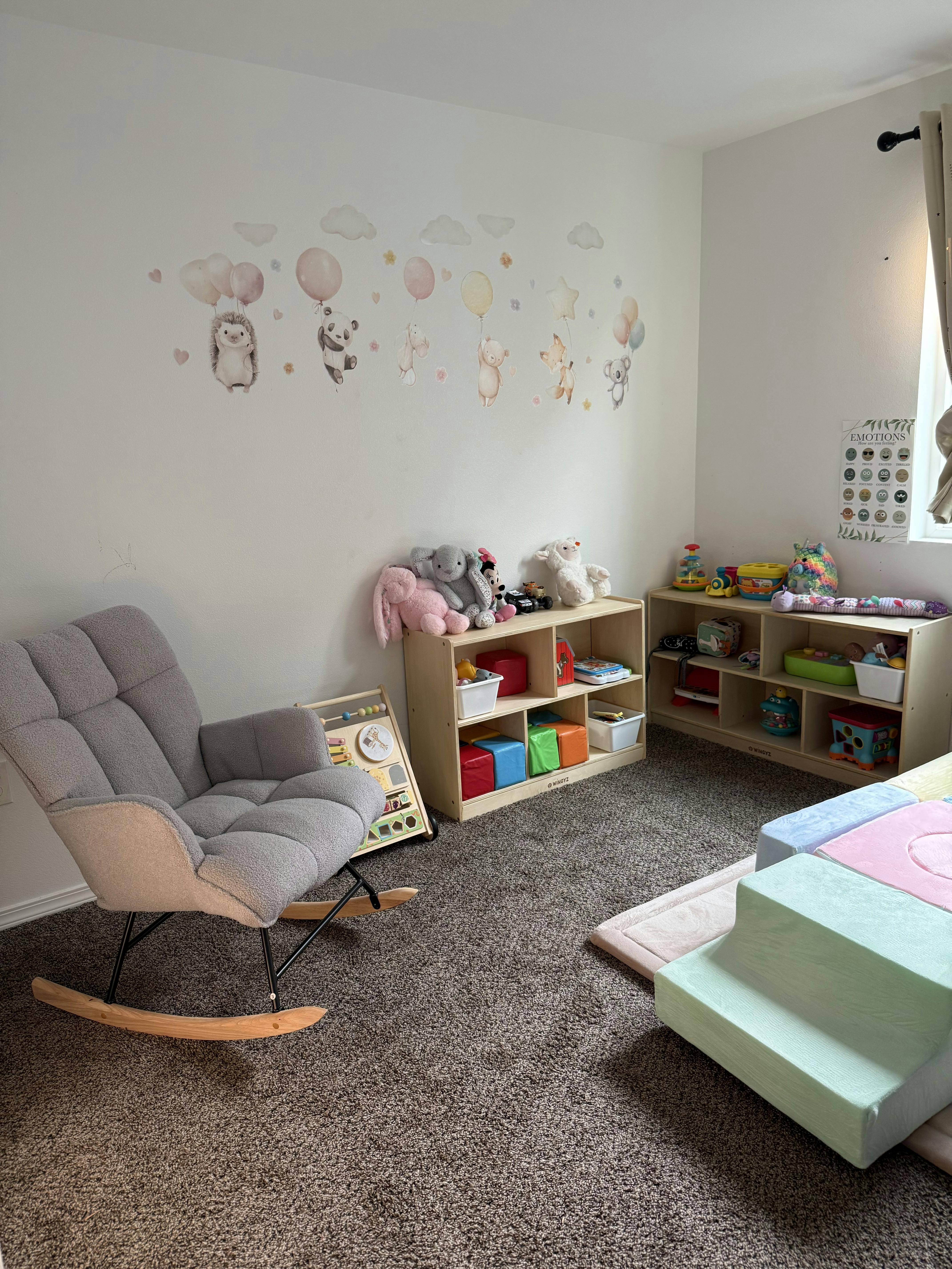 Child playroom with rocking chair, toy storage shelves, and wall decals