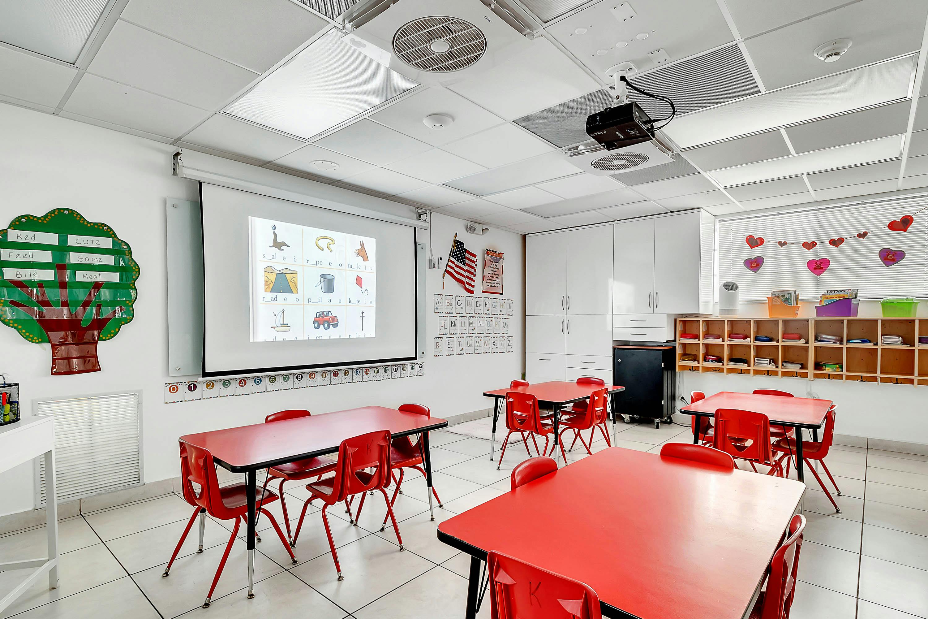 Empty classroom with red tables and chairs, projector screen displaying images