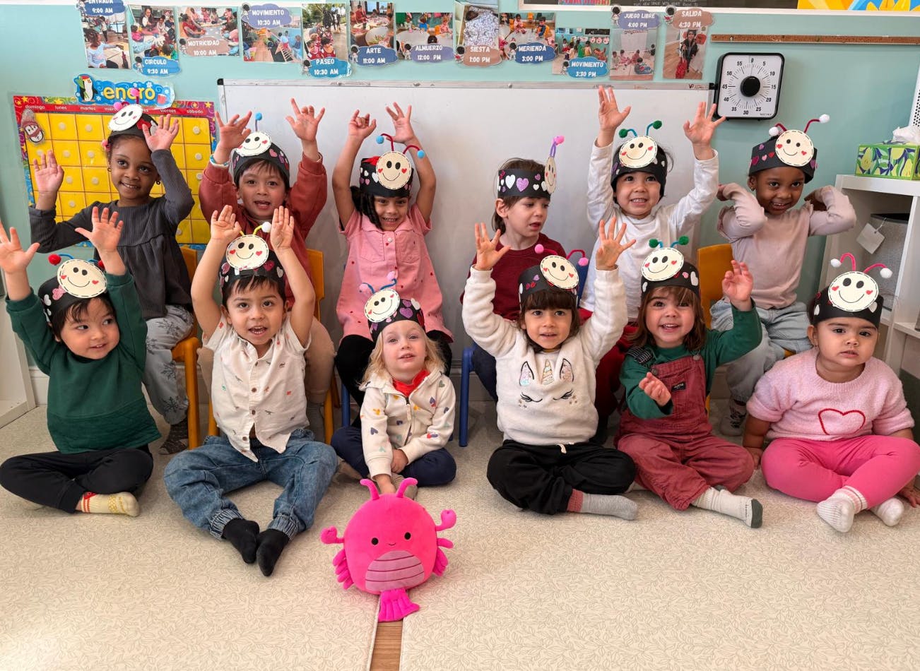 Group of children wearing insect headbands, sitting and raising their hands
