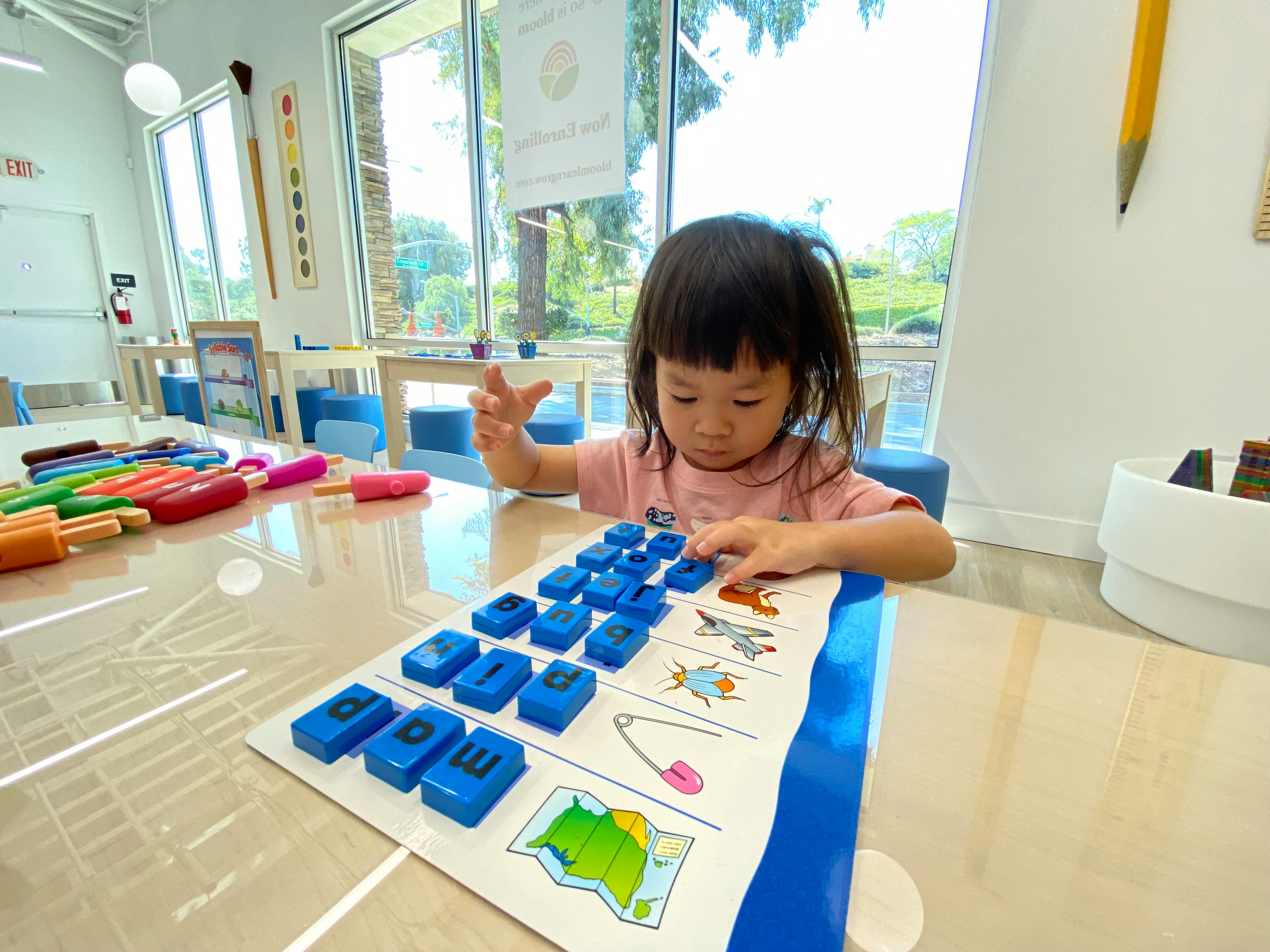 Child playing with blue letter blocks on a learning mat in a classroom