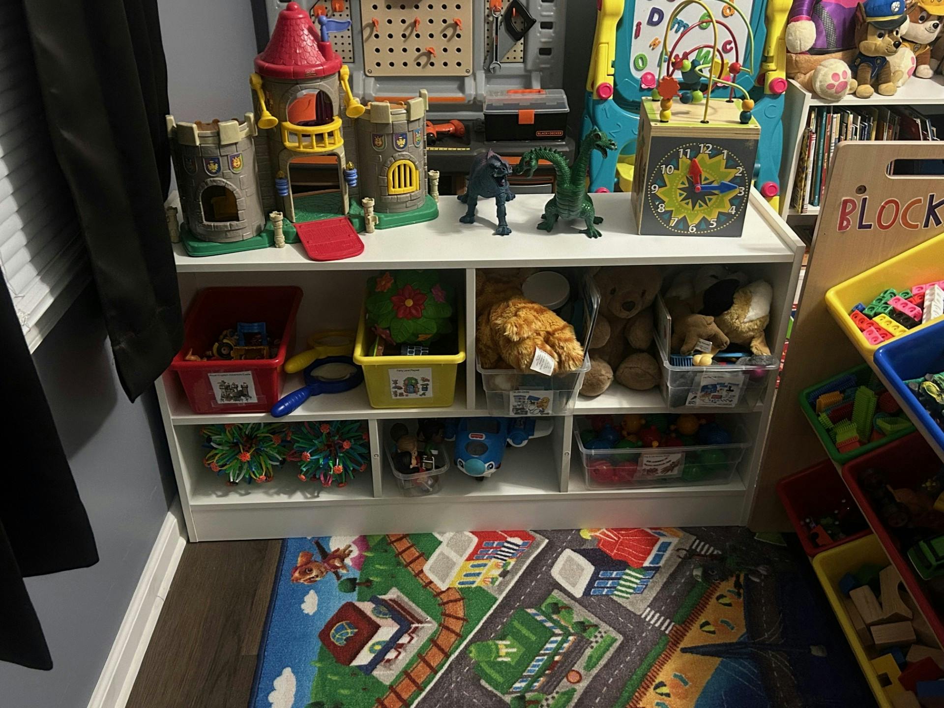 Toy shelf with various toys, including castles, stuffed animals, and bins