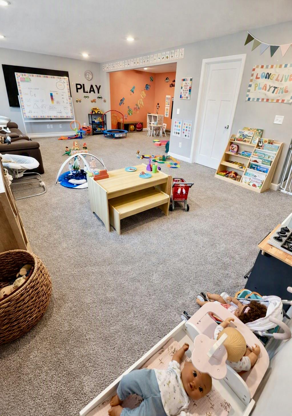 Childcare room with play tables, doll strollers, toys, and educational signs