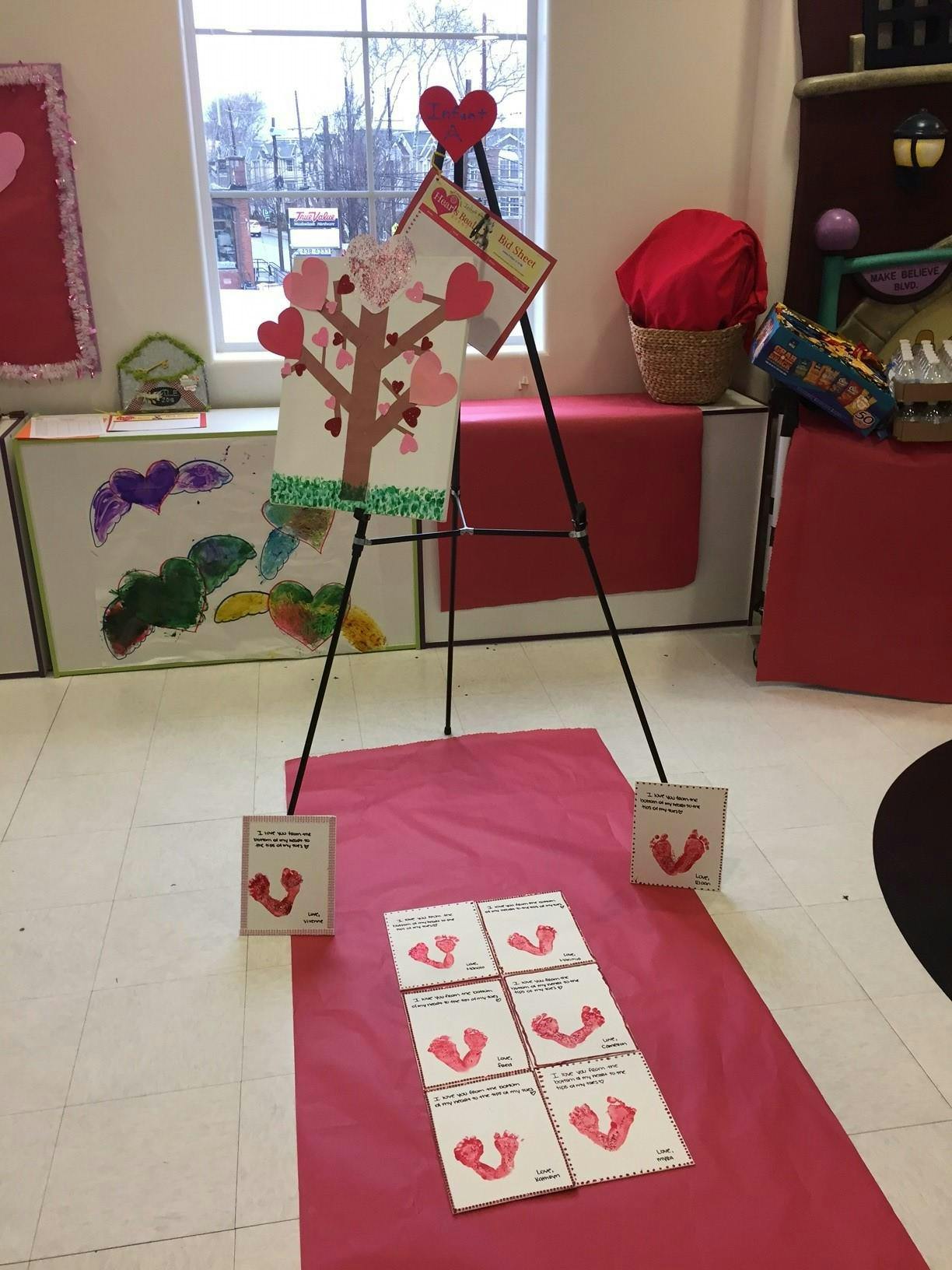 Easel with heart-decorated tree art and cards on a pink mat