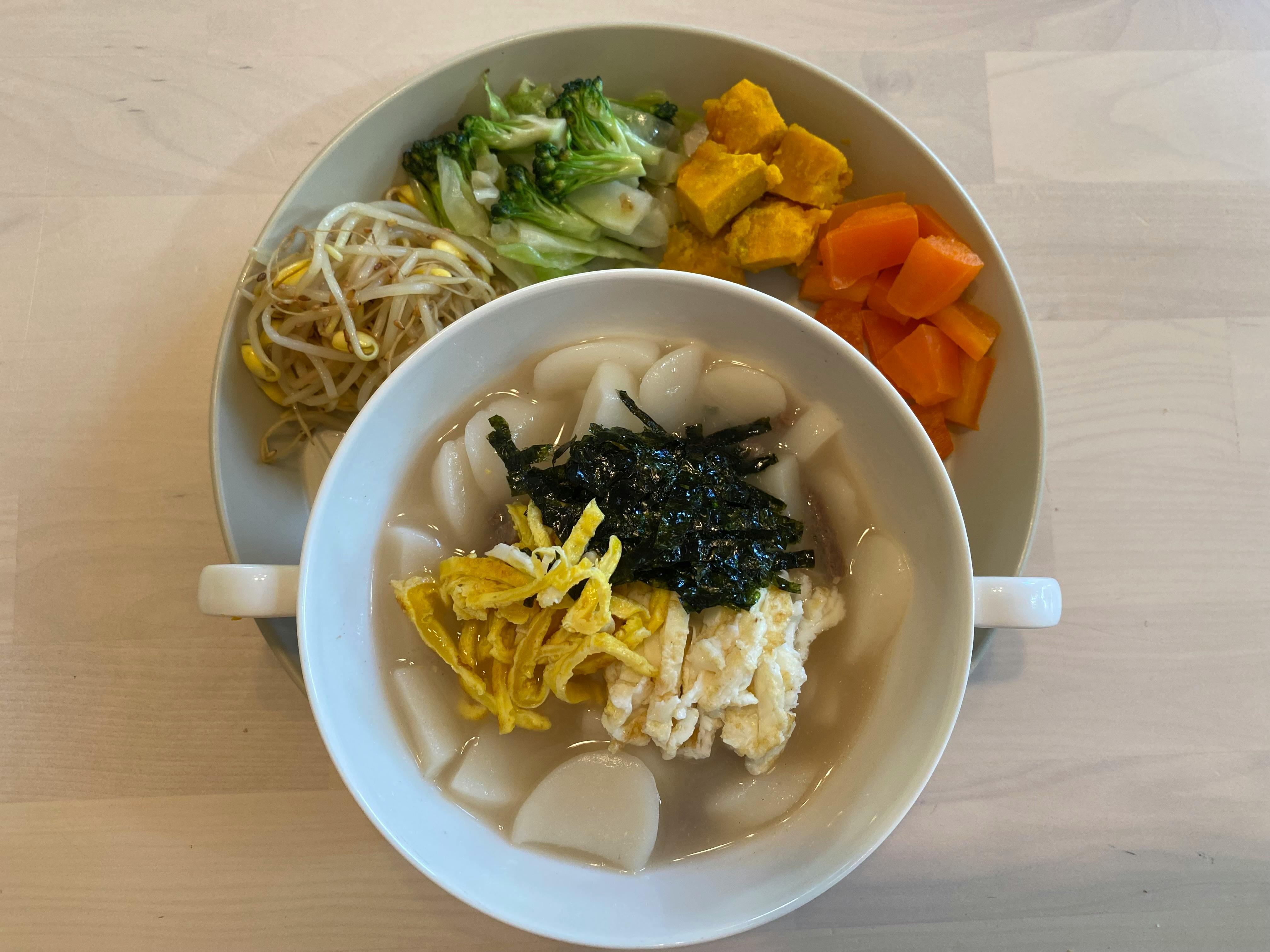 Bowl of tteokguk with side dishes of vegetables