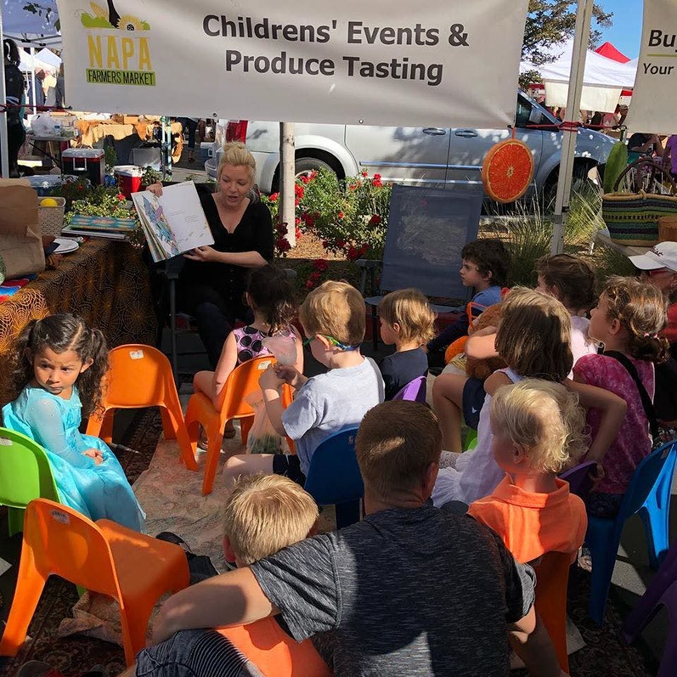 Person reading a book to a group of children sitting on small chairs