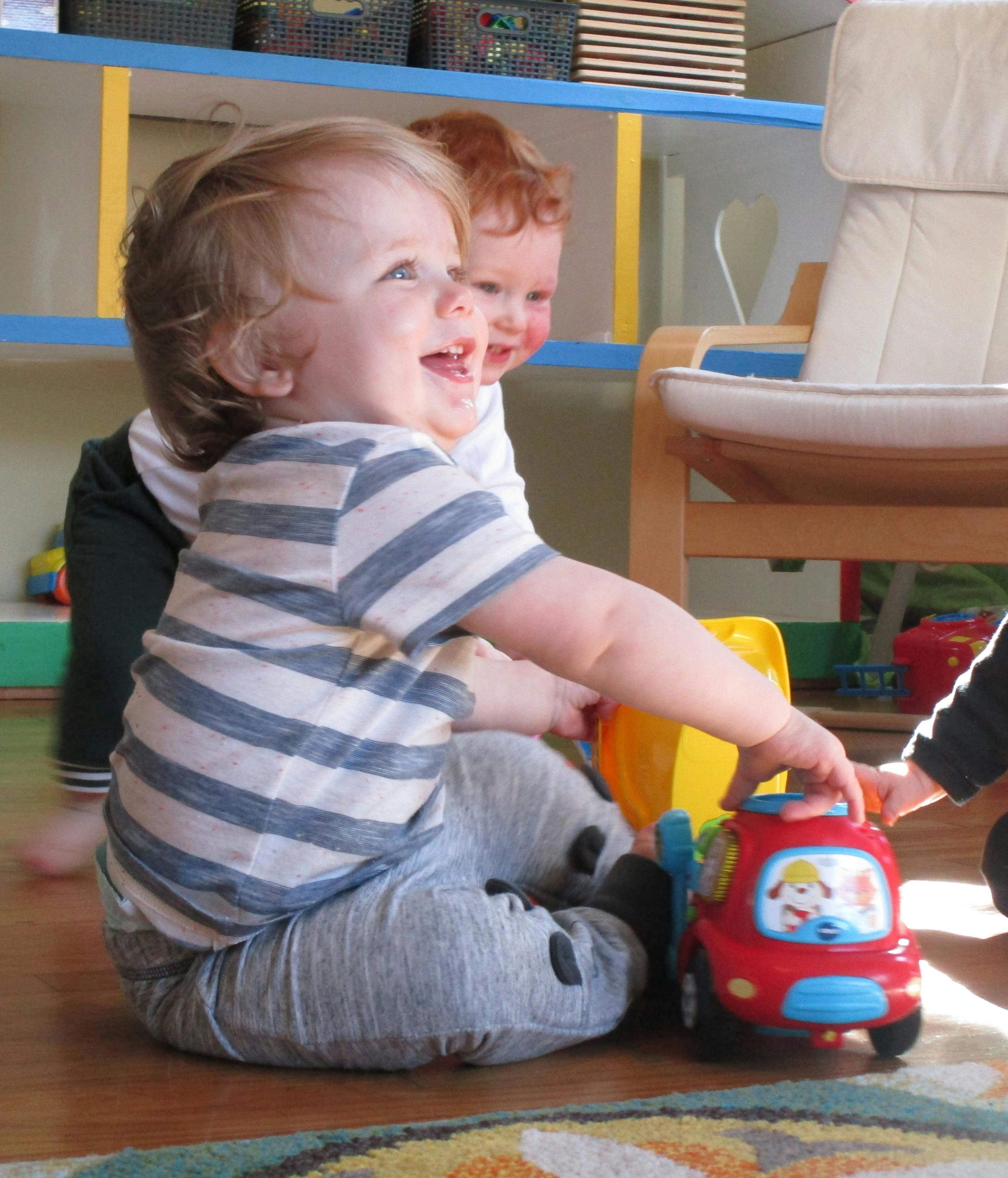 Two children playing with a red toy car on the floor