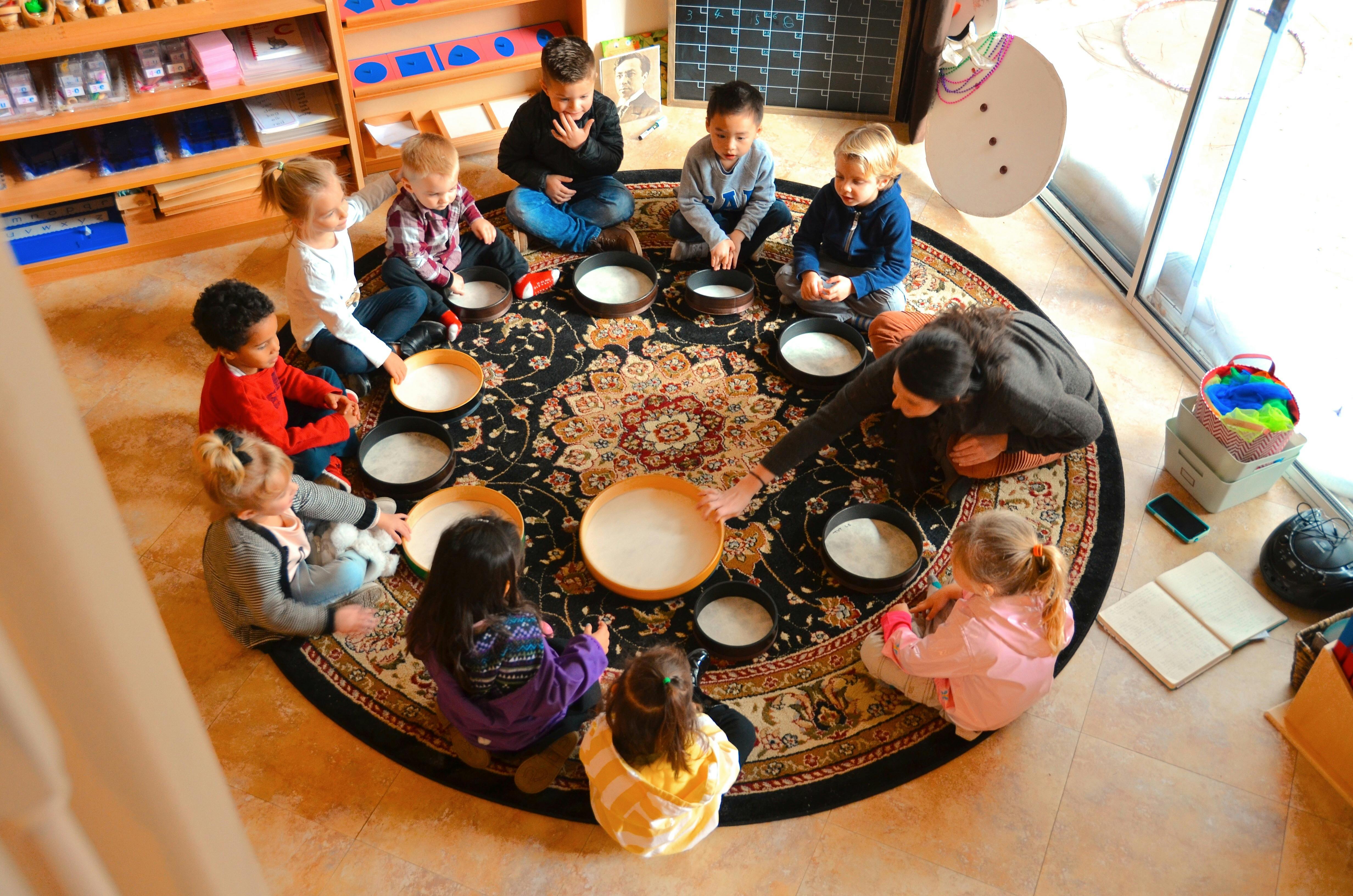 Adult and children sitting in a circle on a rug with bowls