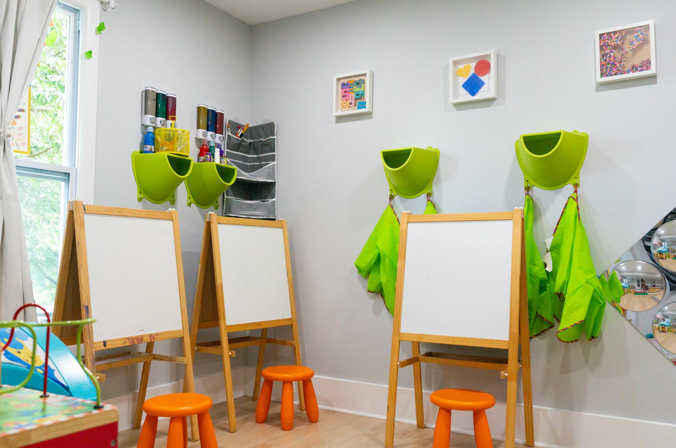 Classroom with multiple easels and orange stools, artwork on the wall