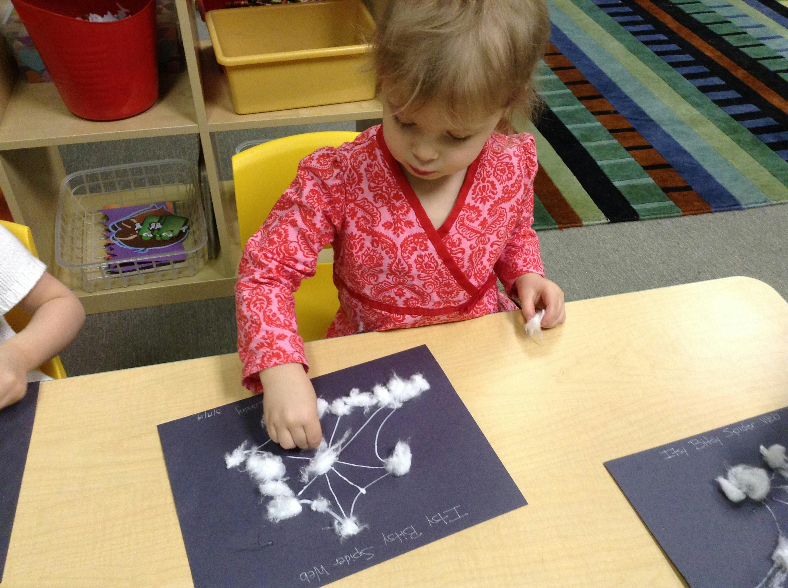 Child crafting an Itsy Bitsy Spider web with cotton balls on black paper