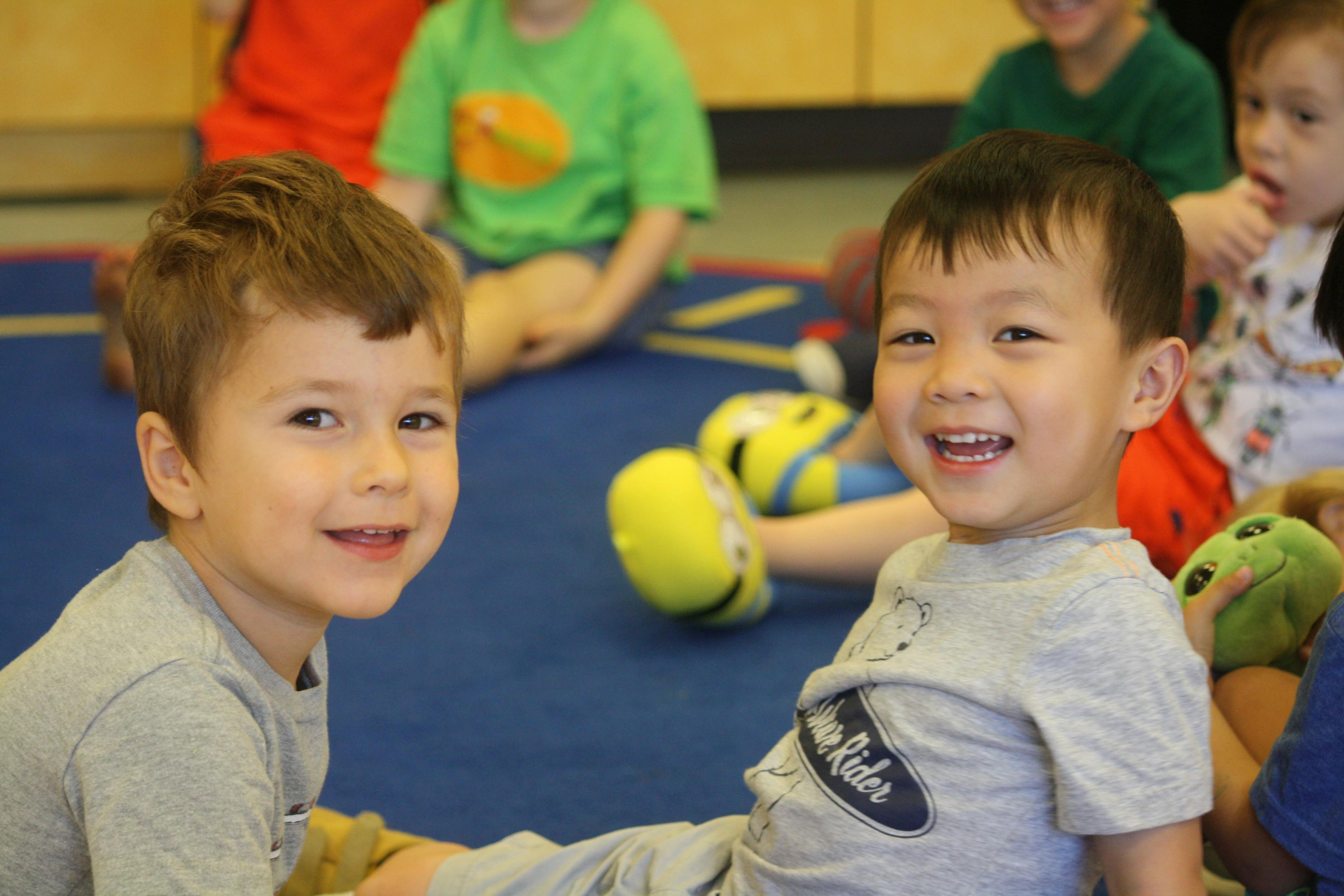 Two children sitting on a blue mat looking at the camera