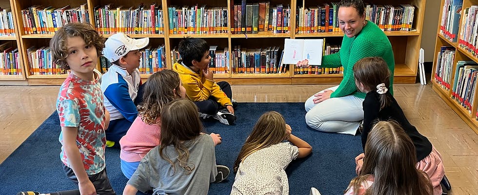 Adult person reading a book to a group of children in a library