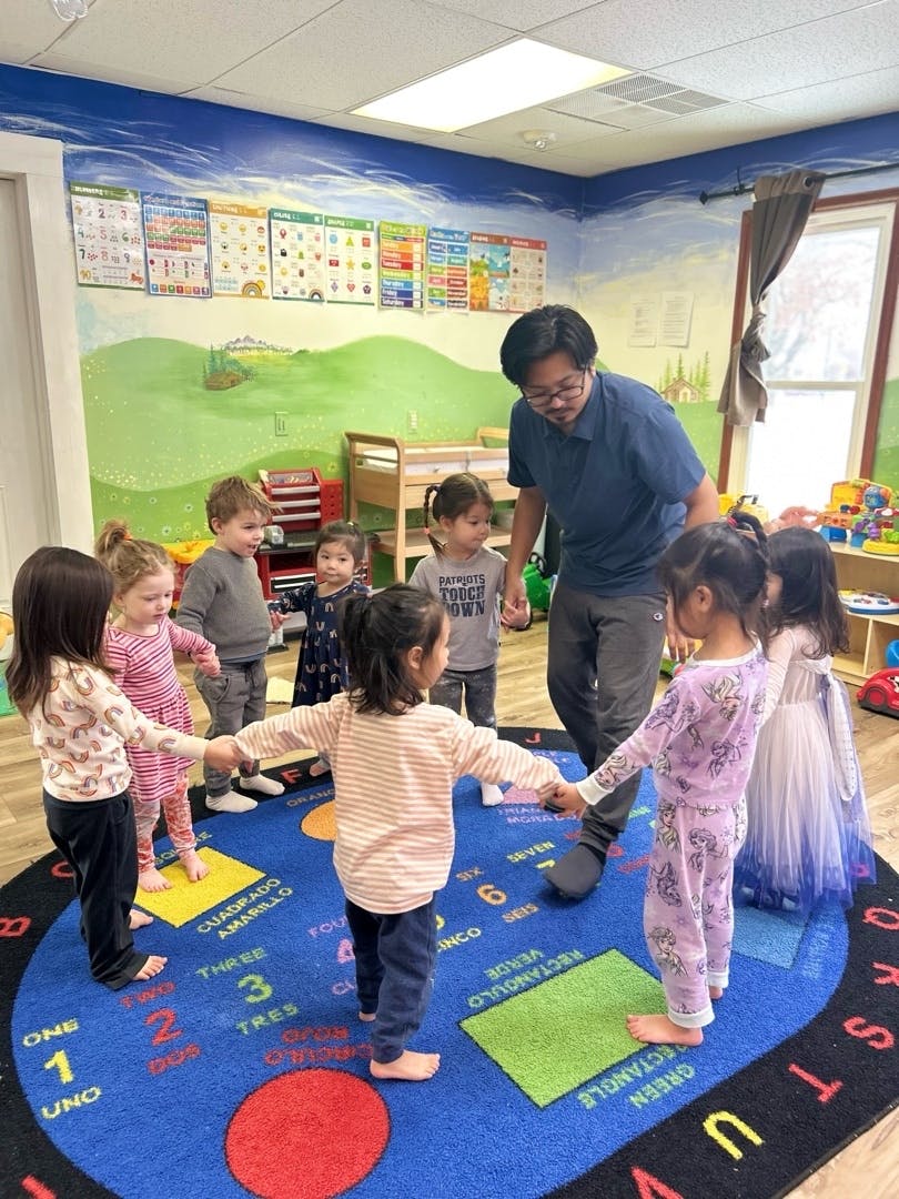 A person holding hands with a group of children in a circle in a classroom