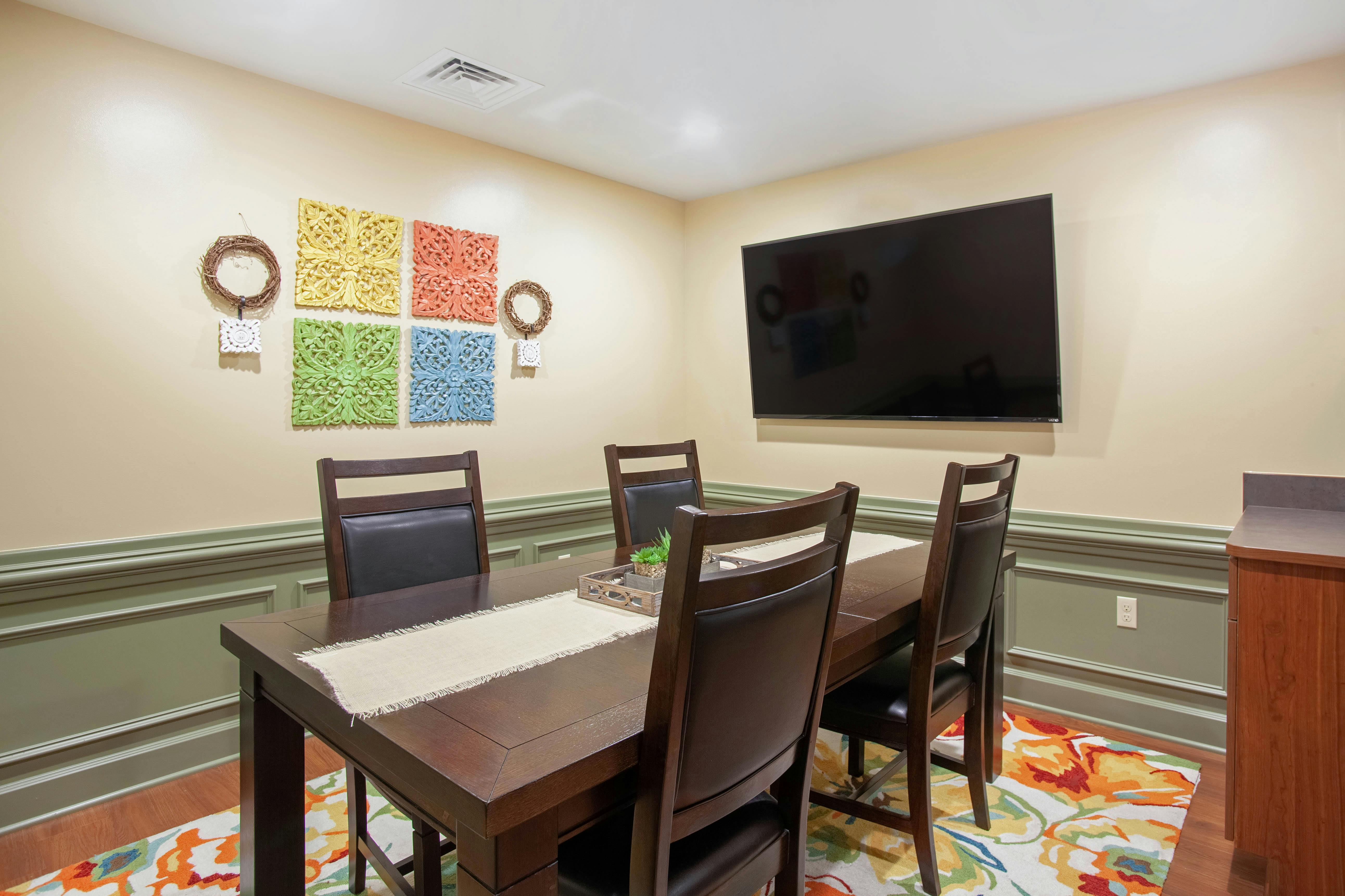 Dining room with a long table, chairs, wall decorations, and a television