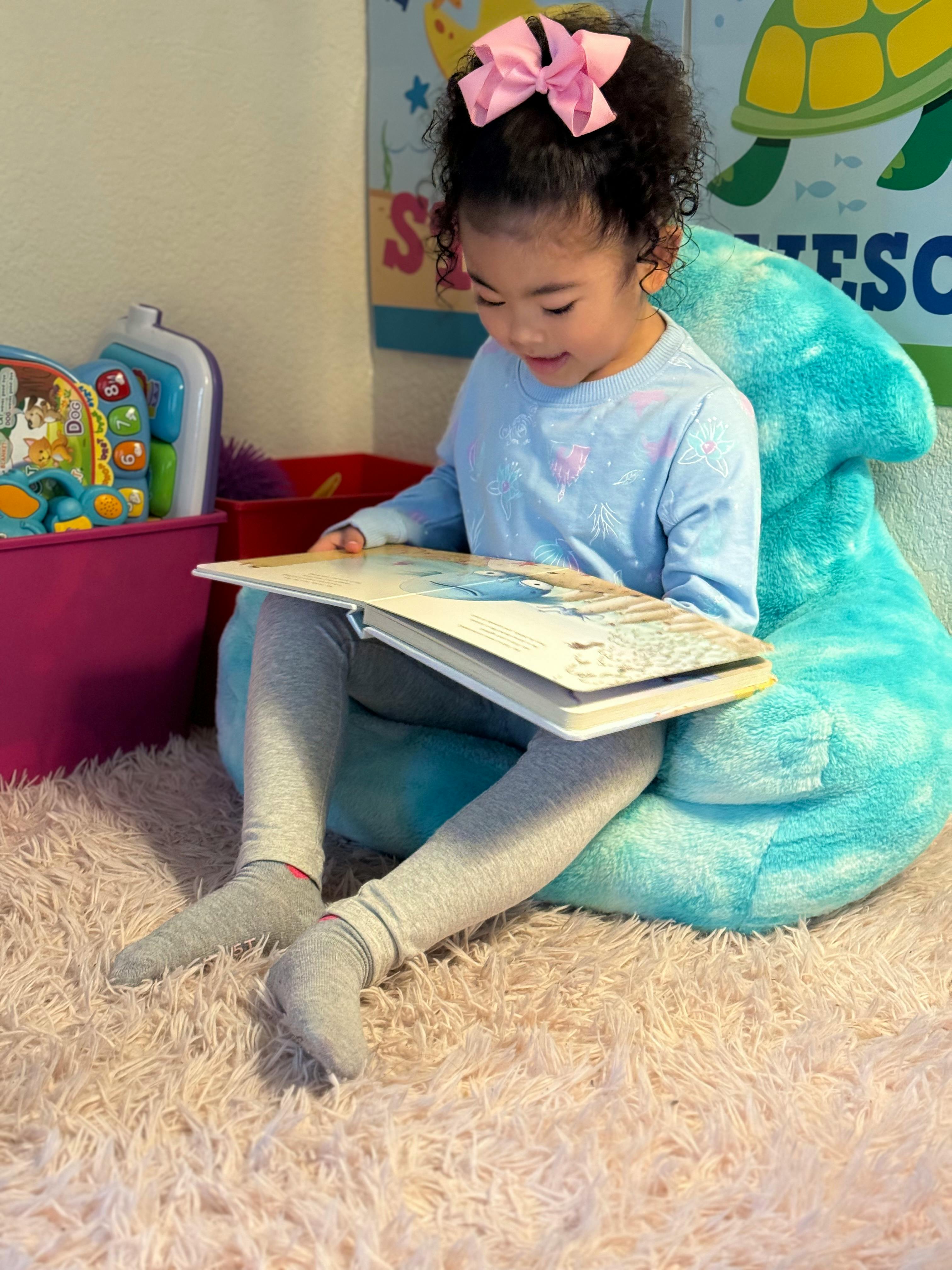 Child sitting on a beanbag chair, reading a book