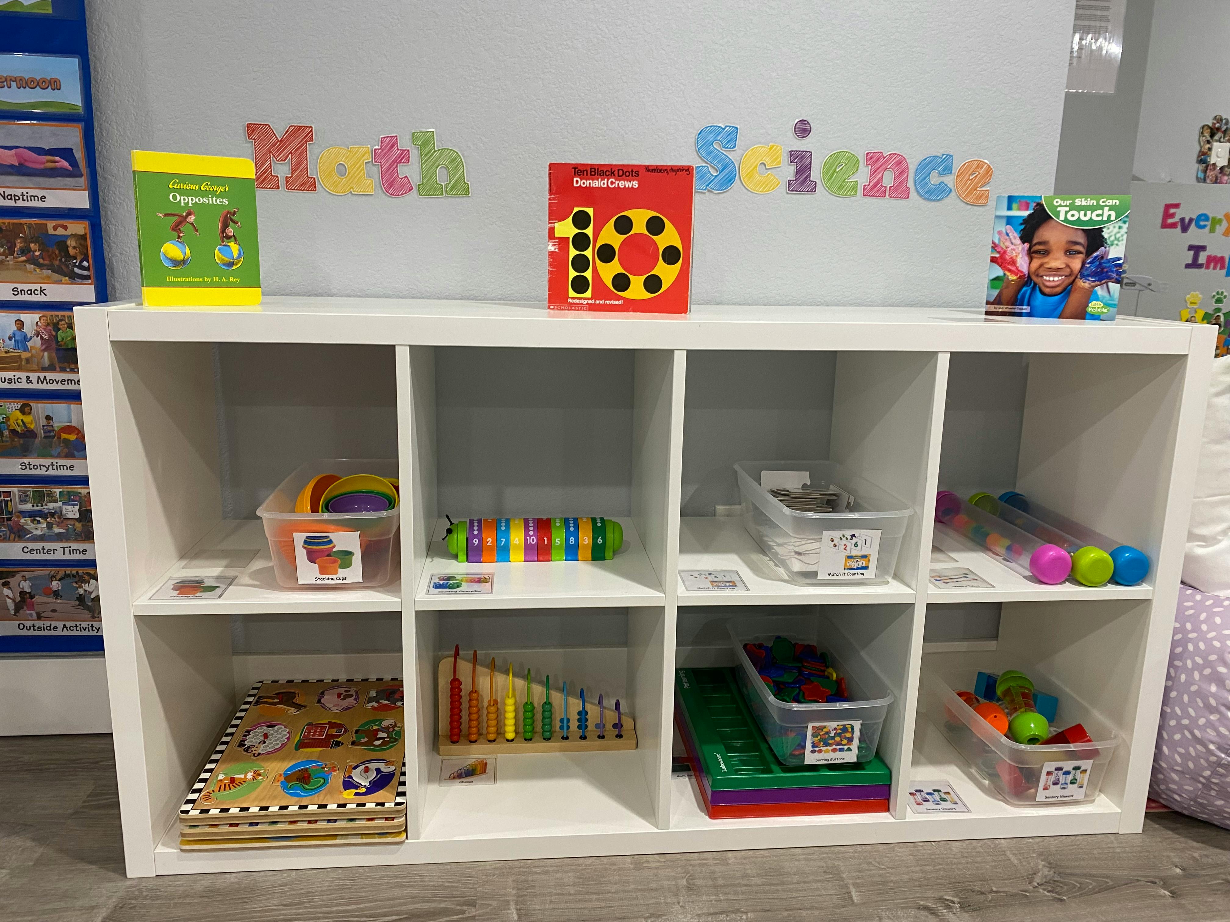 White cubby shelf with children's books, puzzles, counting toys, and sorting bins