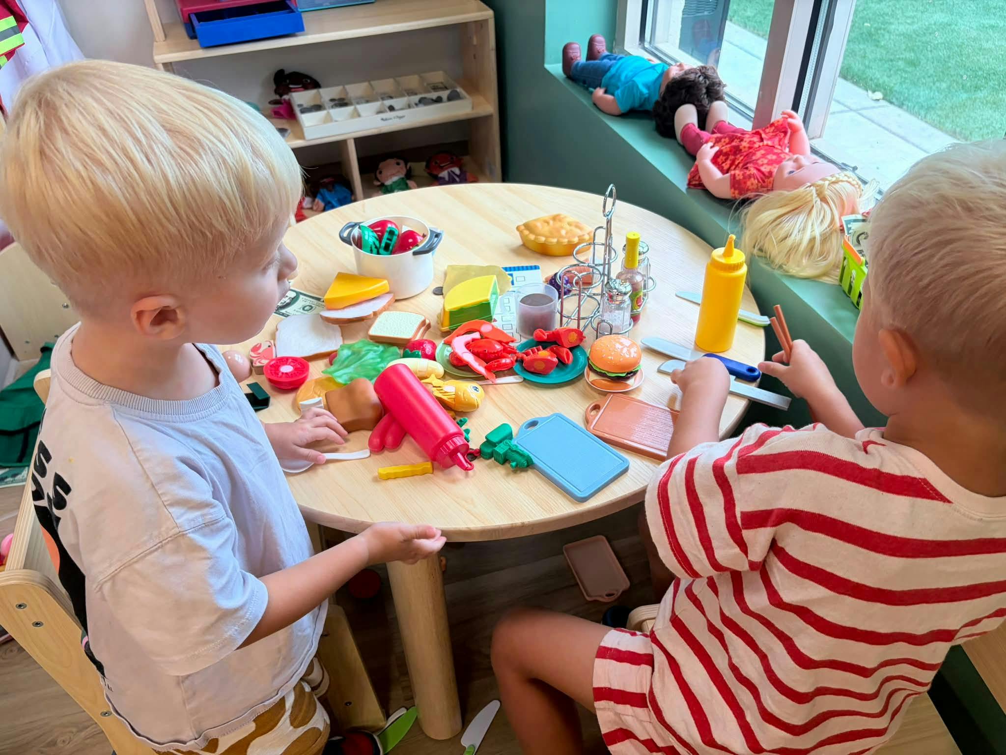 Two children playing with toy food on a small wooden table