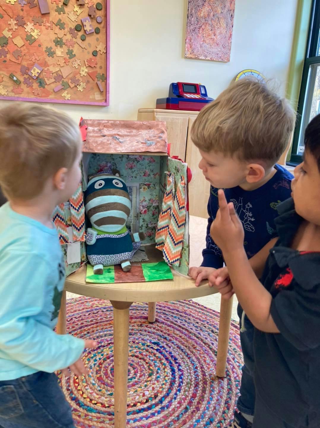 Two children looking at a stuffed animal in a small cardboard house
