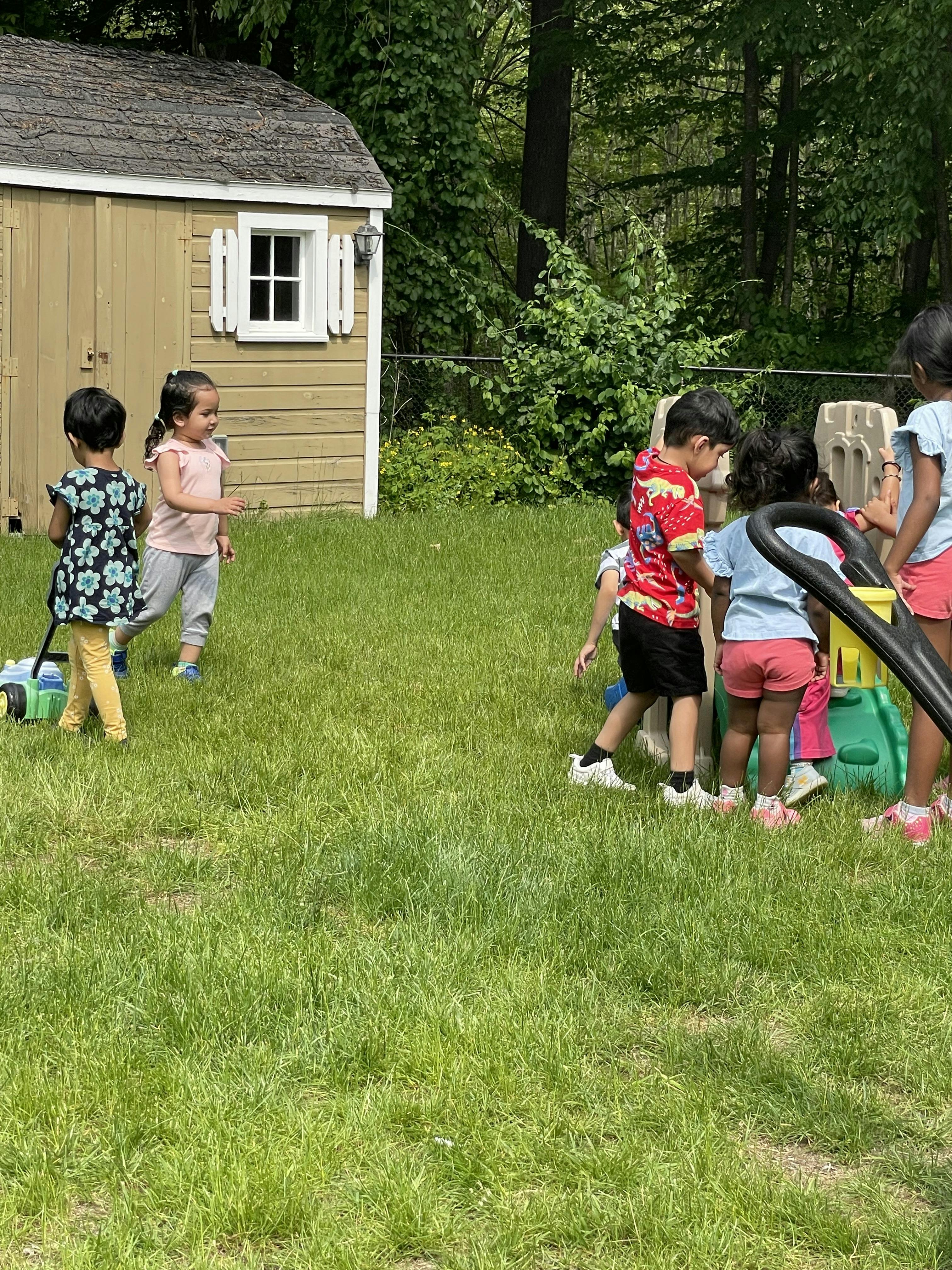 Children playing outdoors on grass near a shed