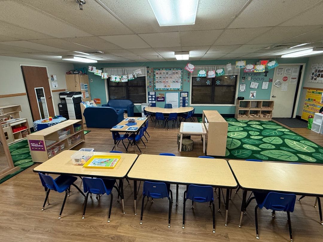 Classroom with small tables and chairs, blue couch, and leaf-patterned rug