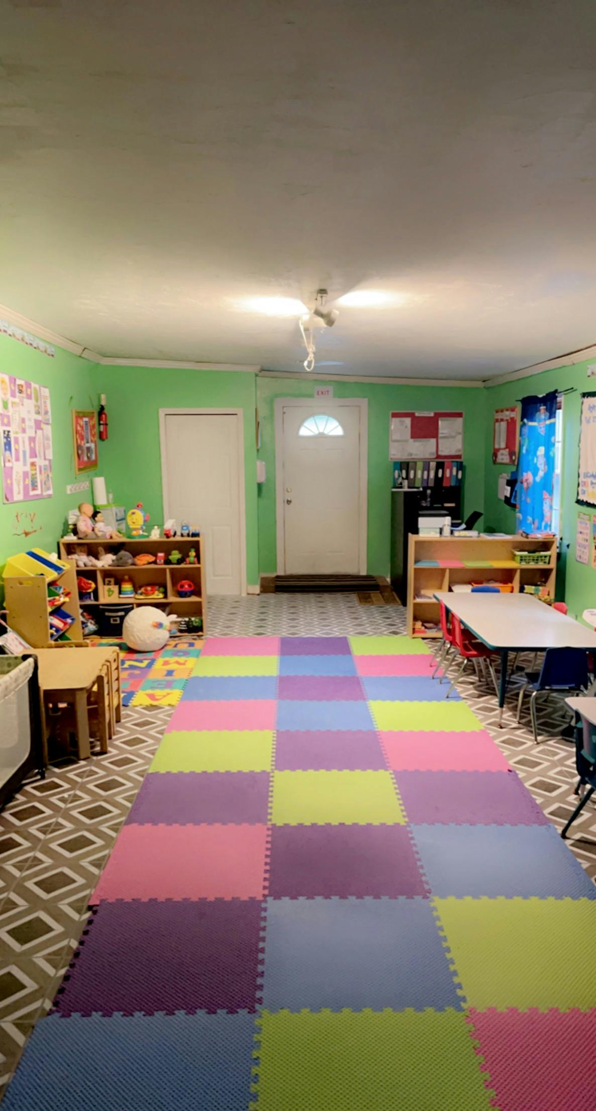 Playroom with colorful floor mats, shelves of toys, and small tables