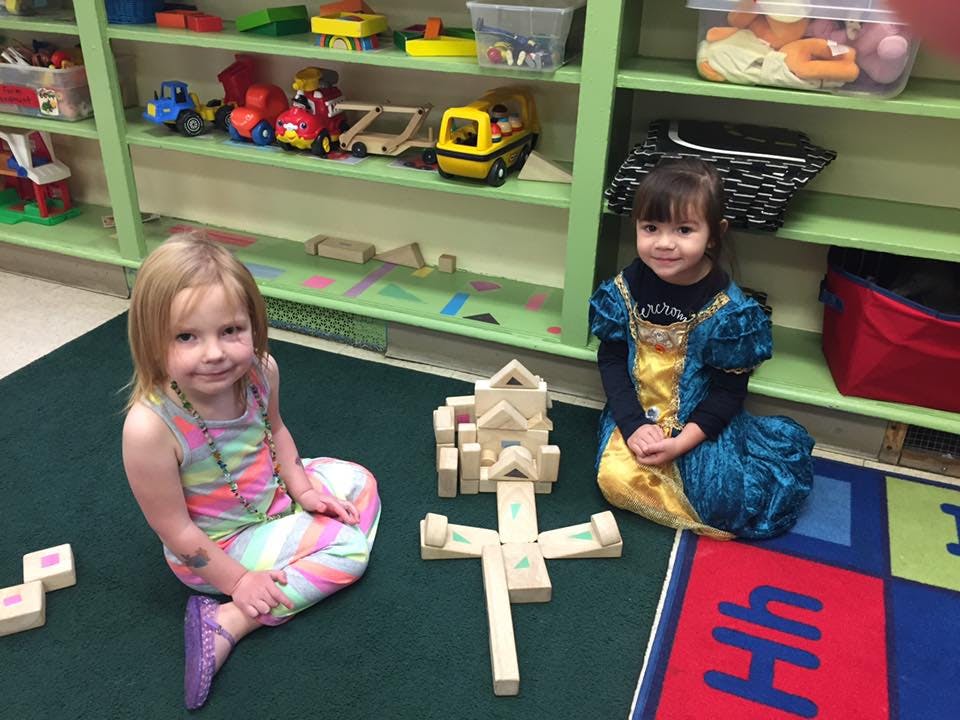 Two children sitting on a rug with wooden blocks