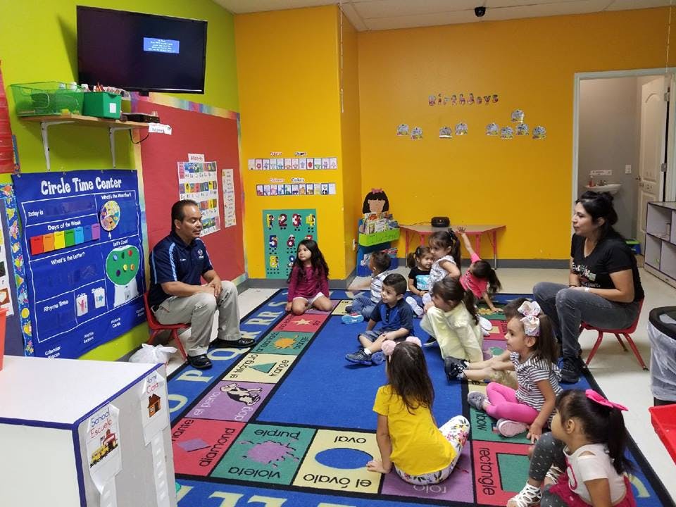 Adults and children sitting on a colorful rug in a classroom