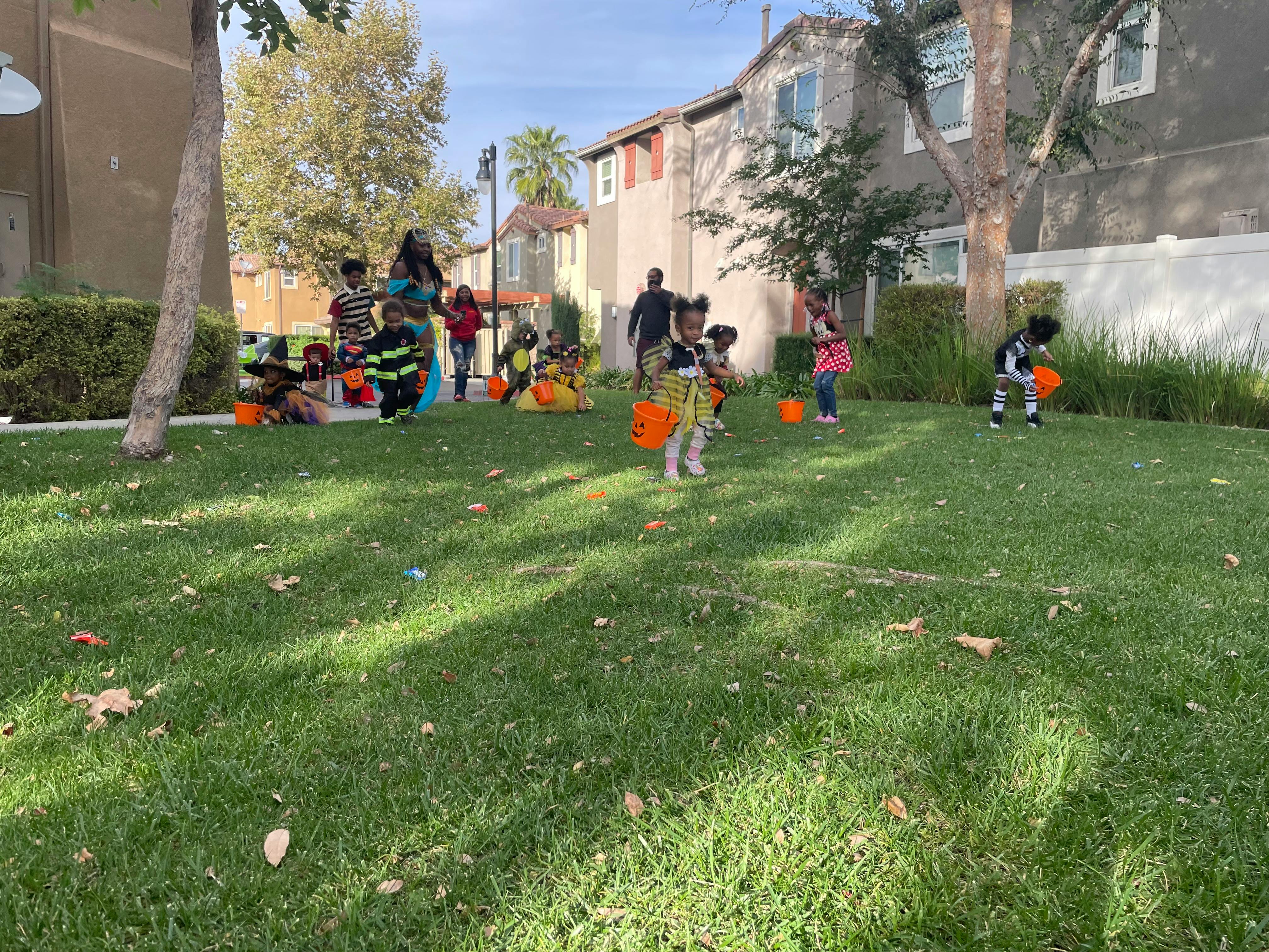 Children in costumes on a grassy lawn with orange buckets