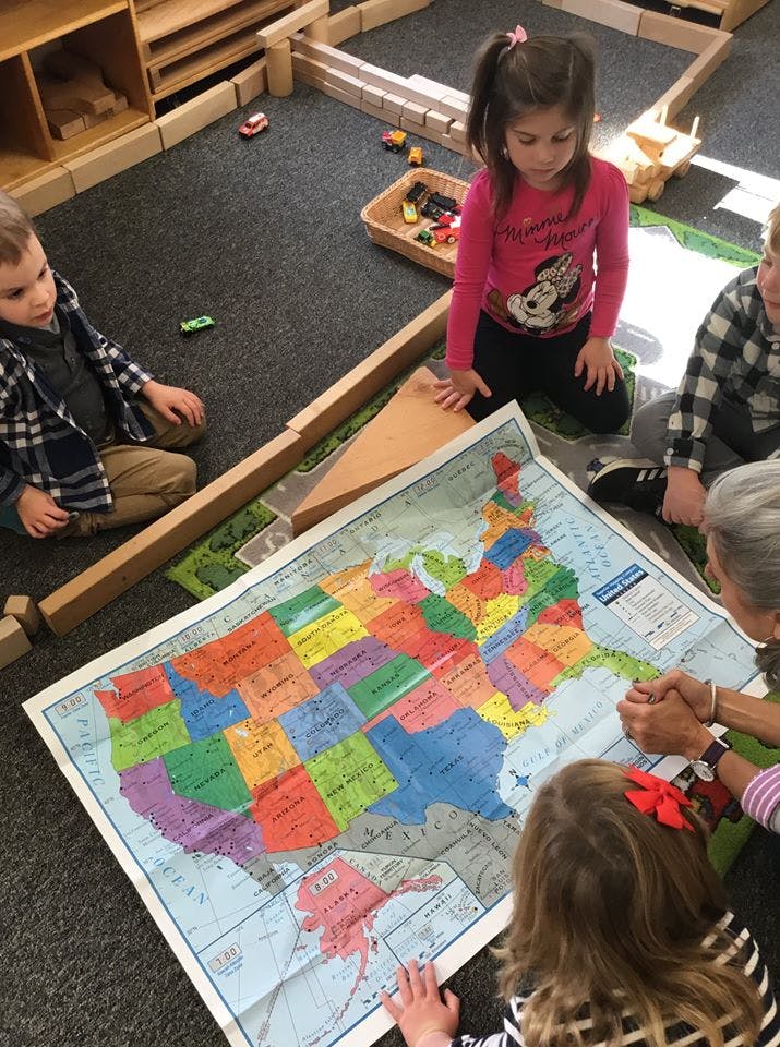Children and an adult looking at a large map of the United States on the floor