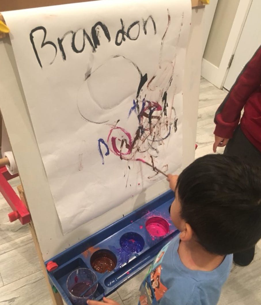 Child painting on an easel with "Brandon" written on the paper