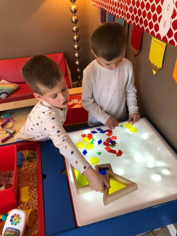 Two children playing with colorful shapes on a light table