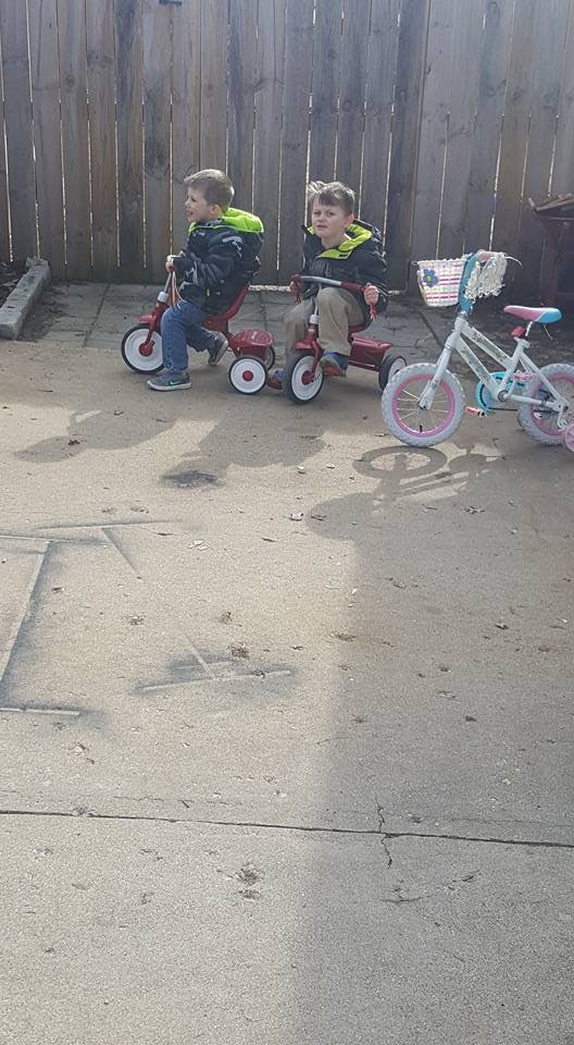 Two children on tricycles next to a small bicycle