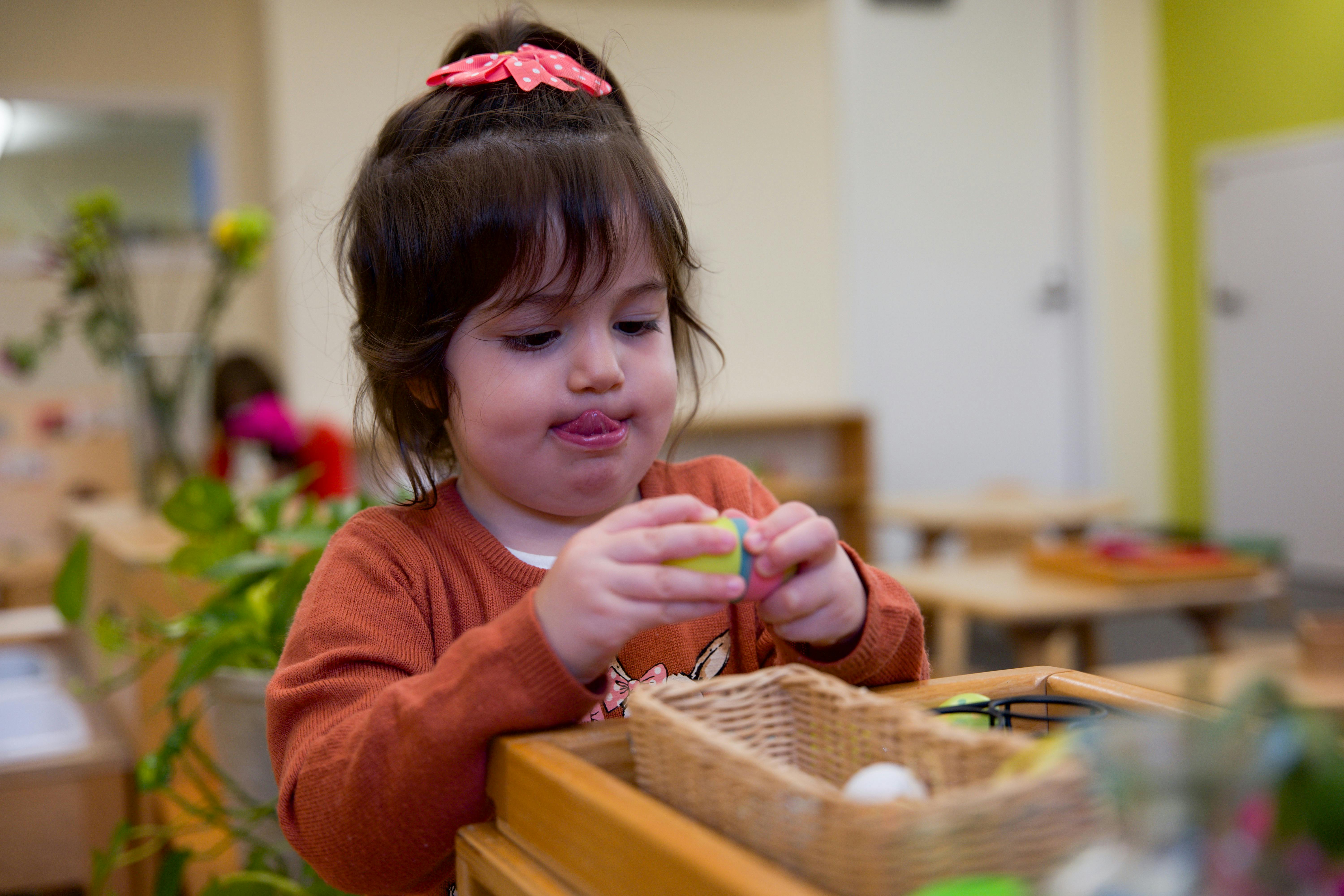 Child holding a small object over a basket in a classroom