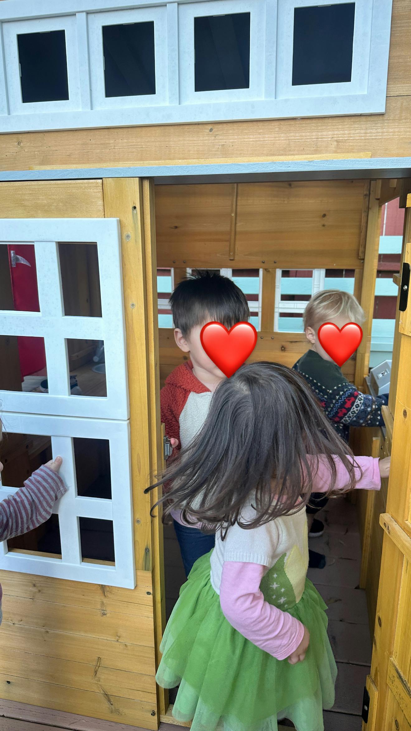 Three children playing inside a wooden playhouse