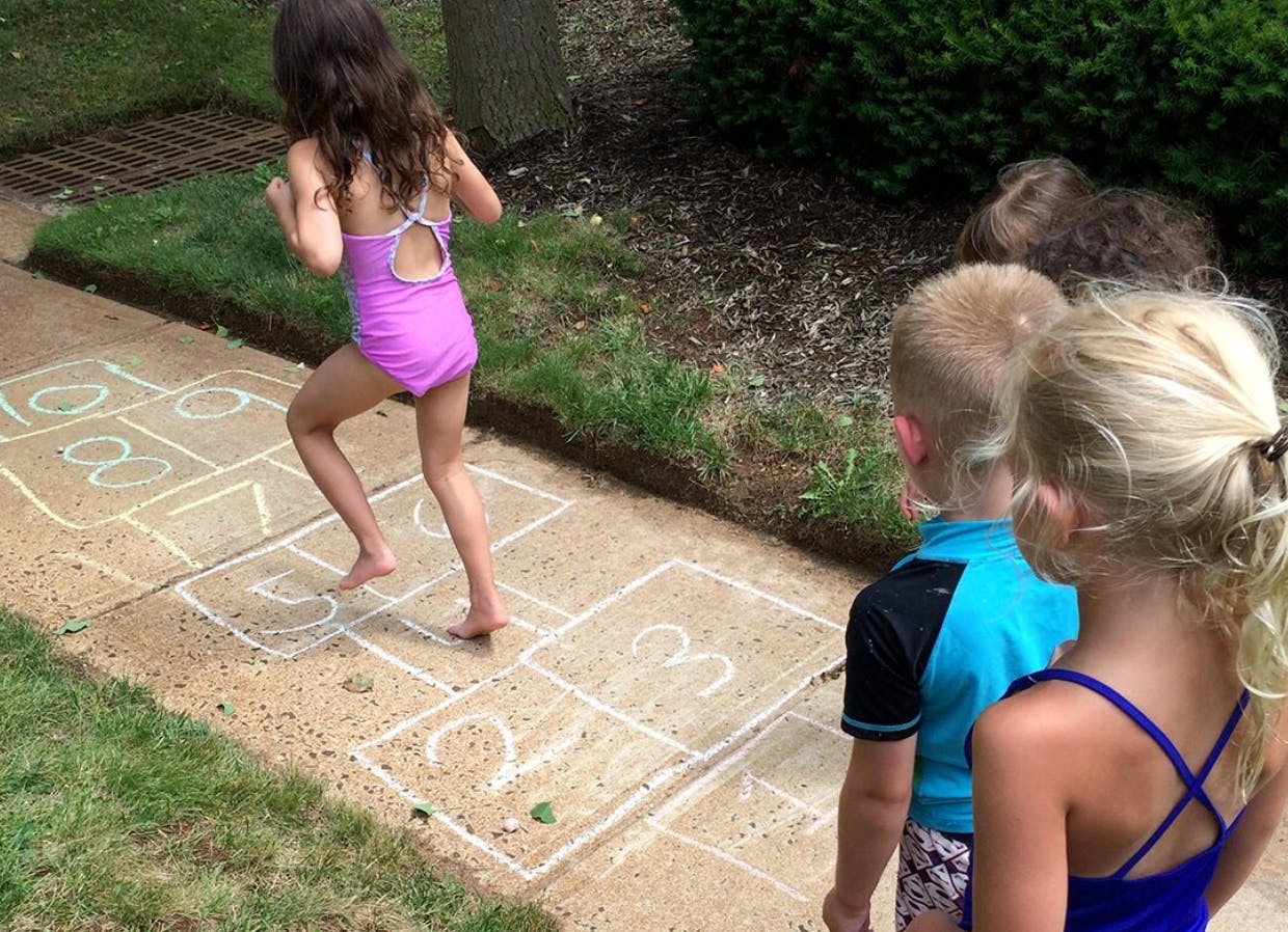 Child playing hopscotch on a sidewalk with other children watching