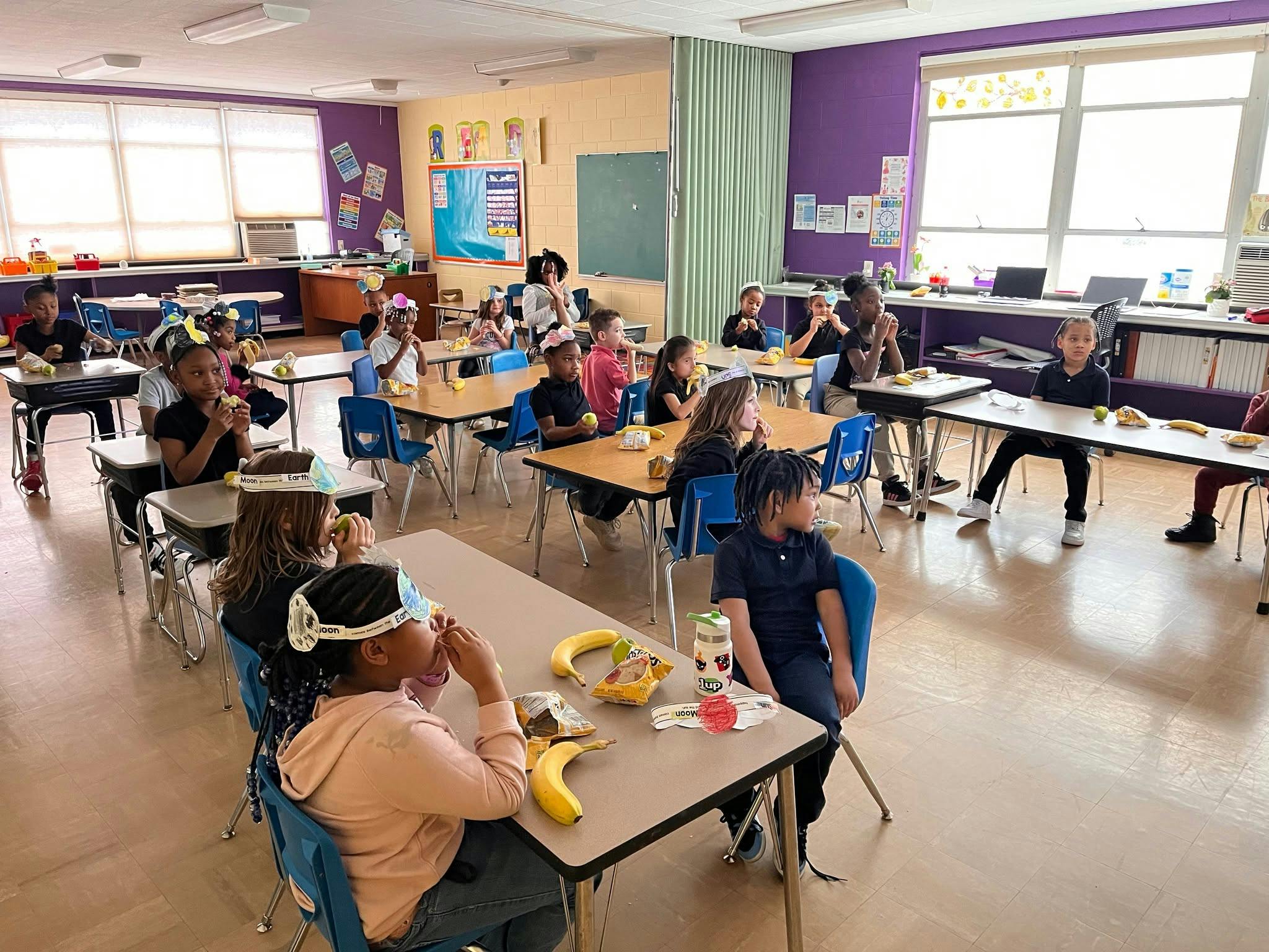 Children wearing paper crowns eating at desks in a classroom