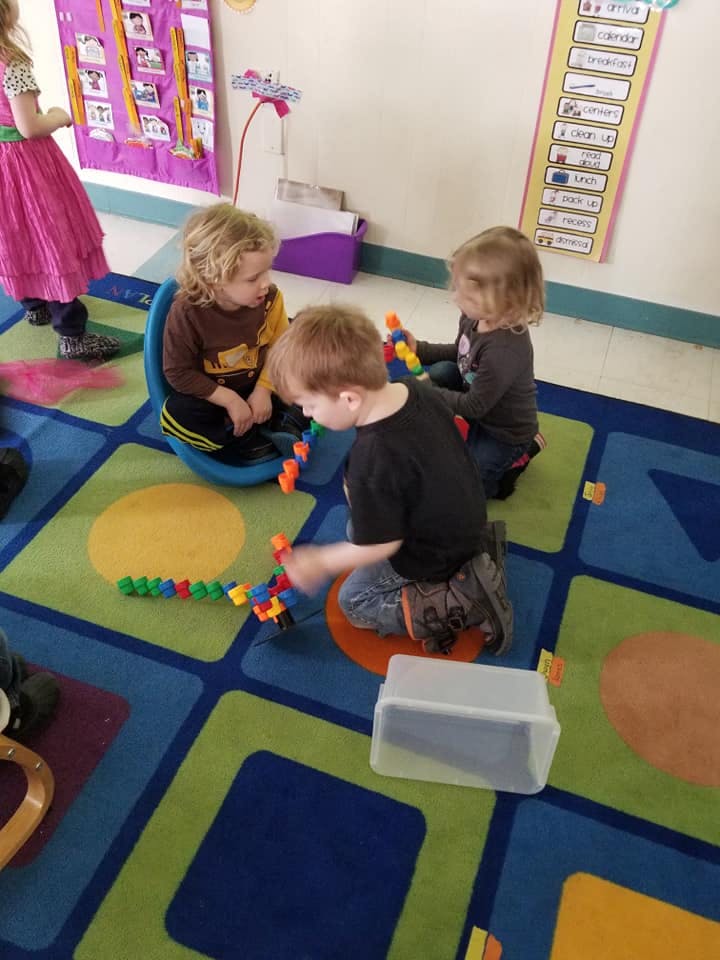 Three children playing with colorful building blocks on a patterned rug
