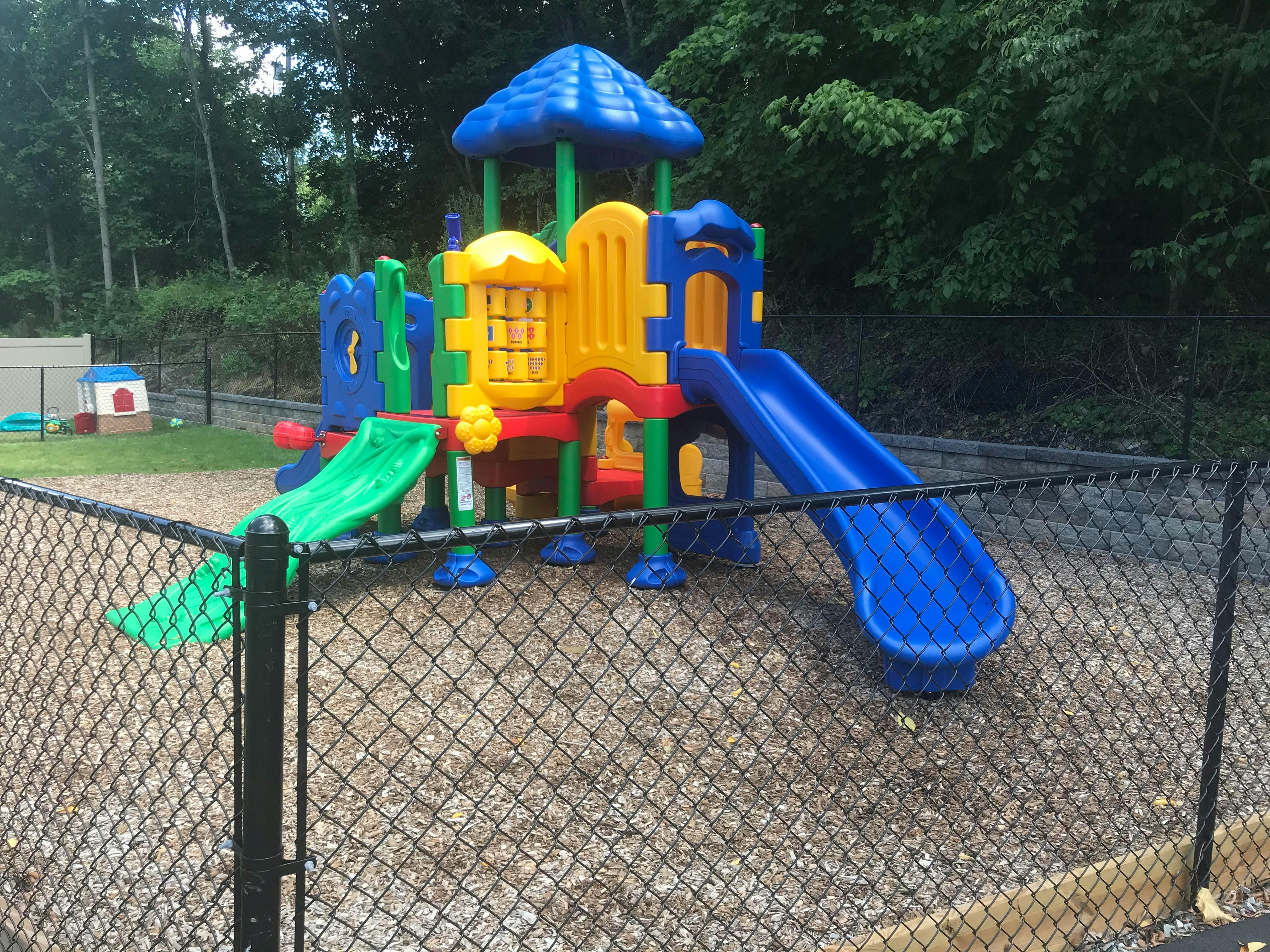 Colorful plastic playset with two slides in a fenced playground area