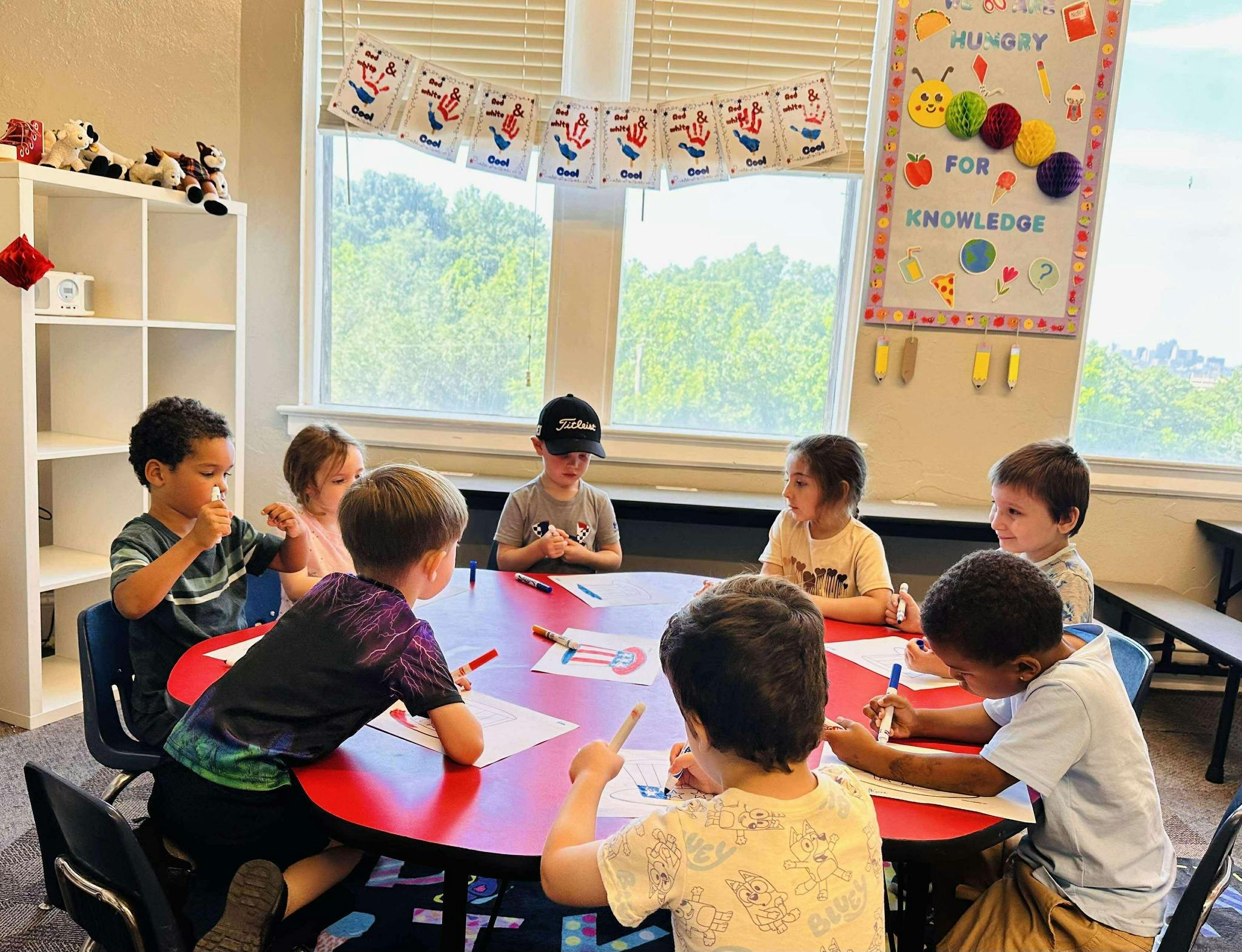Children sitting around a red table drawing and coloring