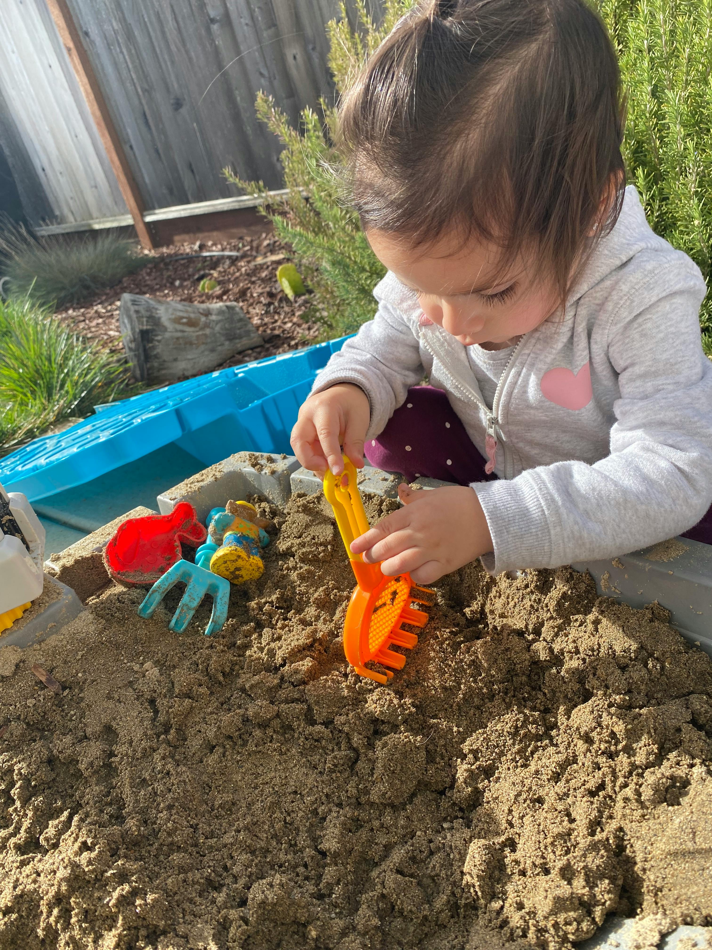 Child playing in a sandbox with a toy rake