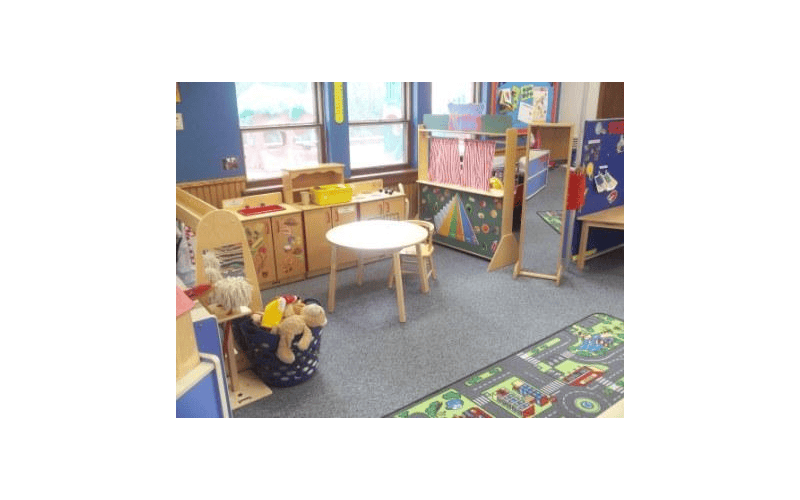 A classroom with a play kitchen, a puppet theater, a table, and a rug with a road map