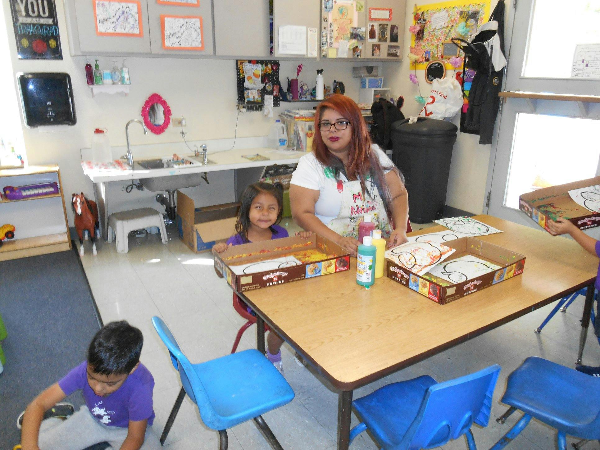 Adult and child at a table with art supplies in a classroom