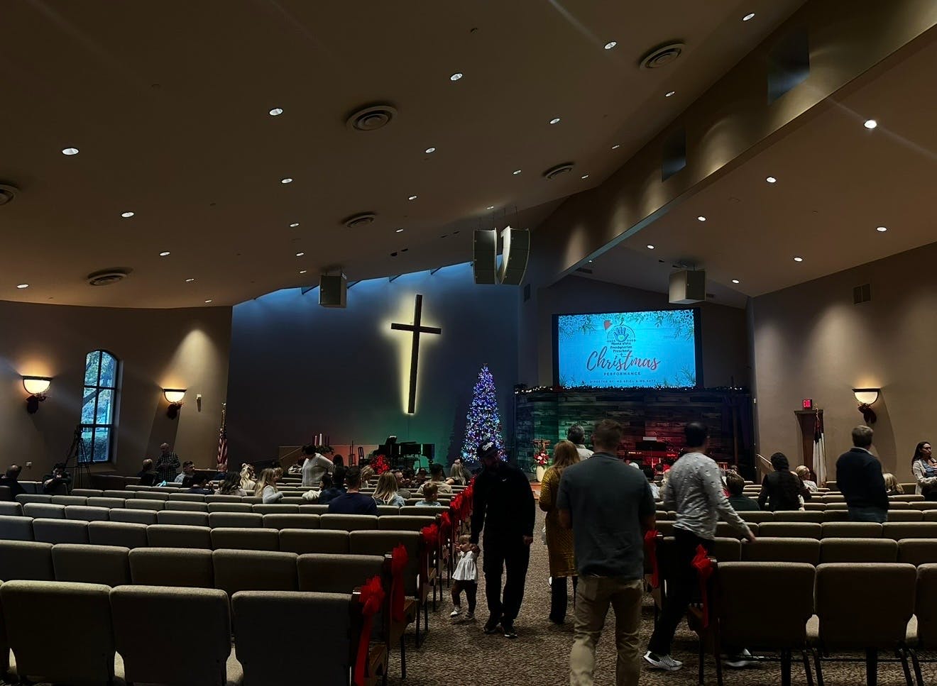People walking into a church auditorium with a large cross and Christmas tree on stage