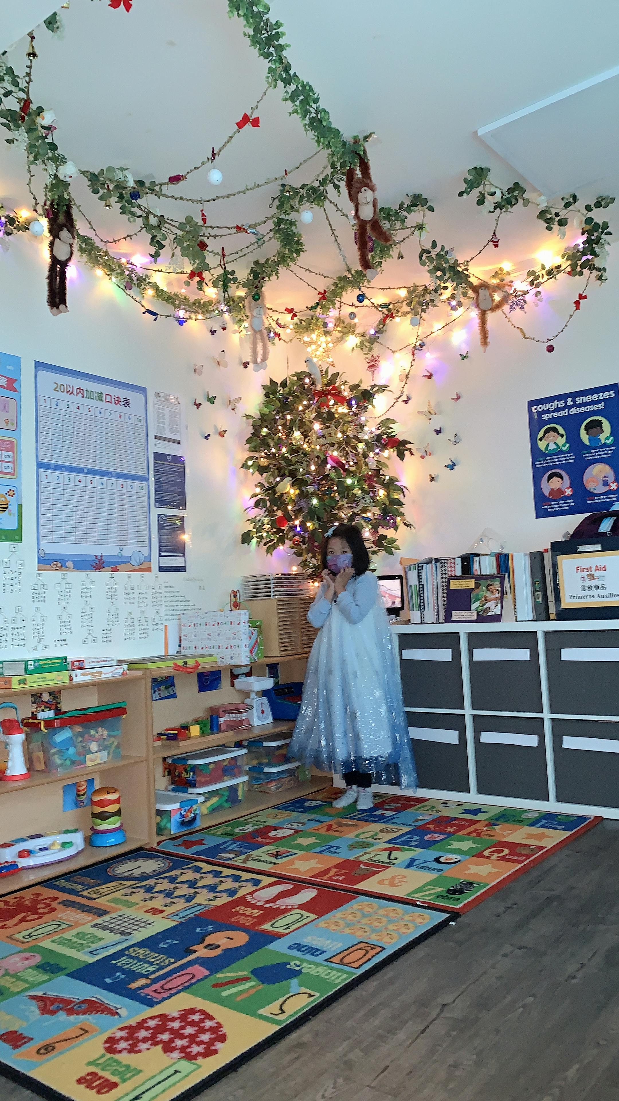 Child in a classroom with a decorated Christmas tree and colorful rug
